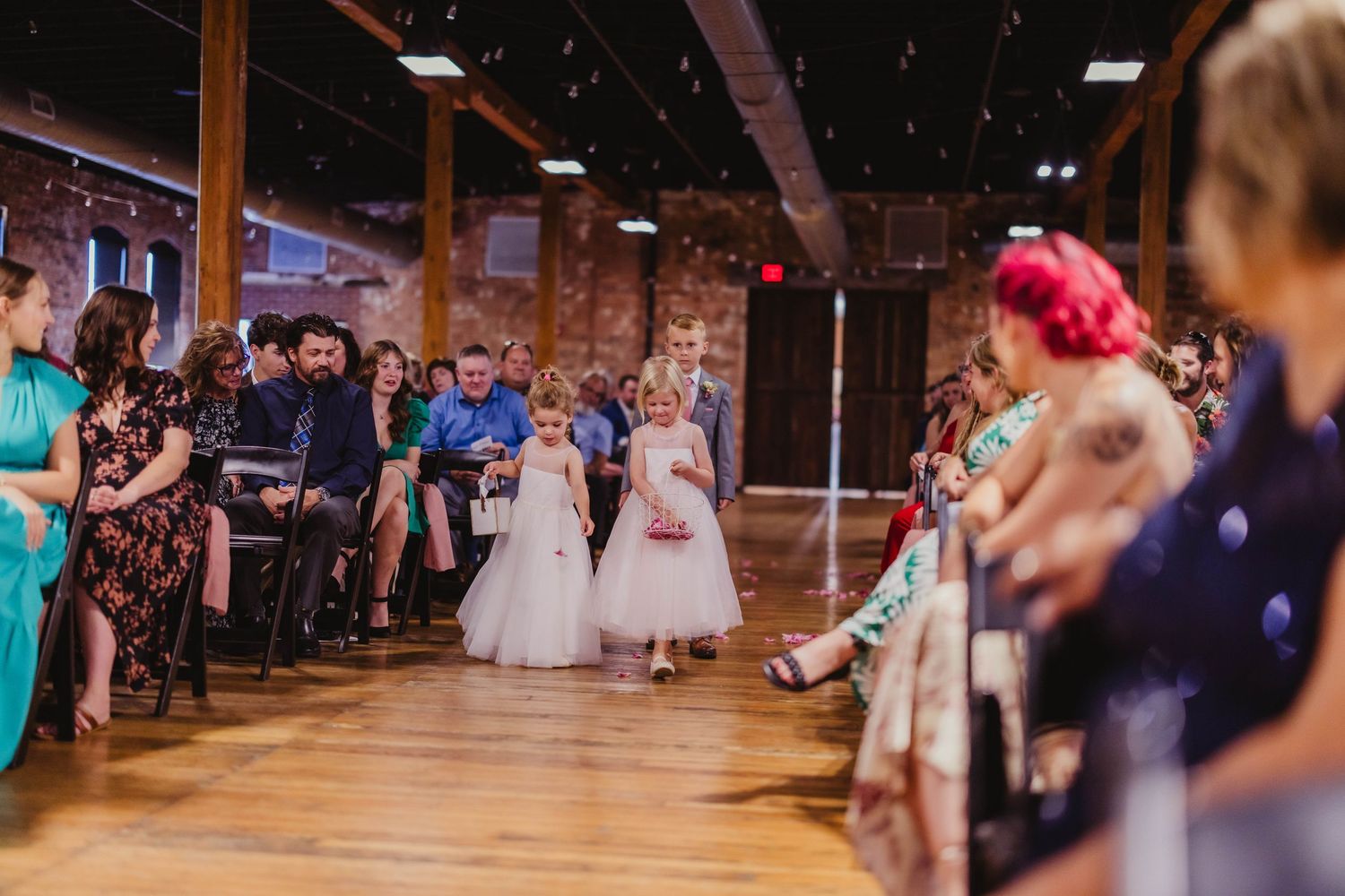 Flower girls in white dresses walk down the aisle during a wedding ceremony in a historic venue.