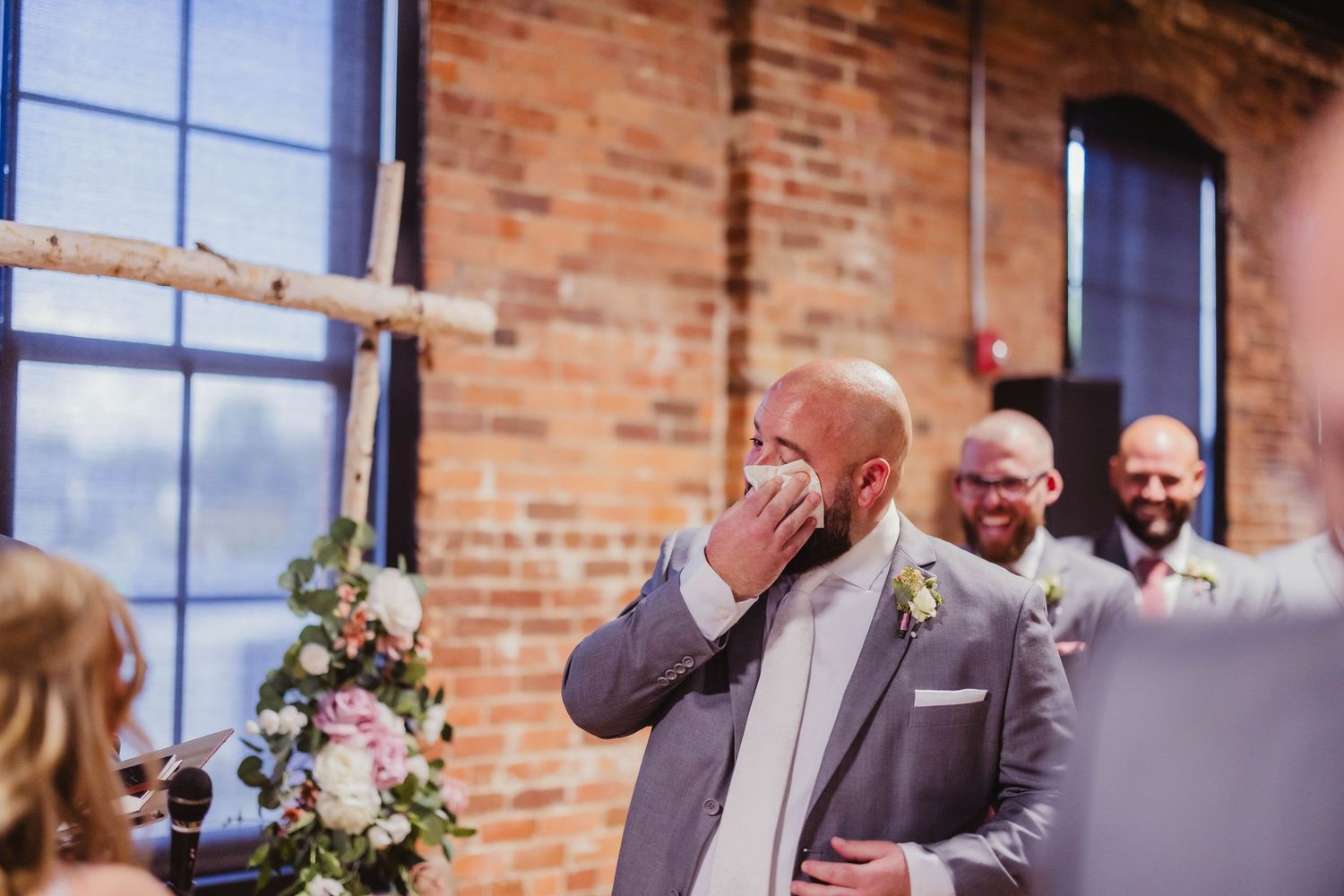 Emotional reaction during wedding ceremony in industrial-style venue with exposed brick walls.