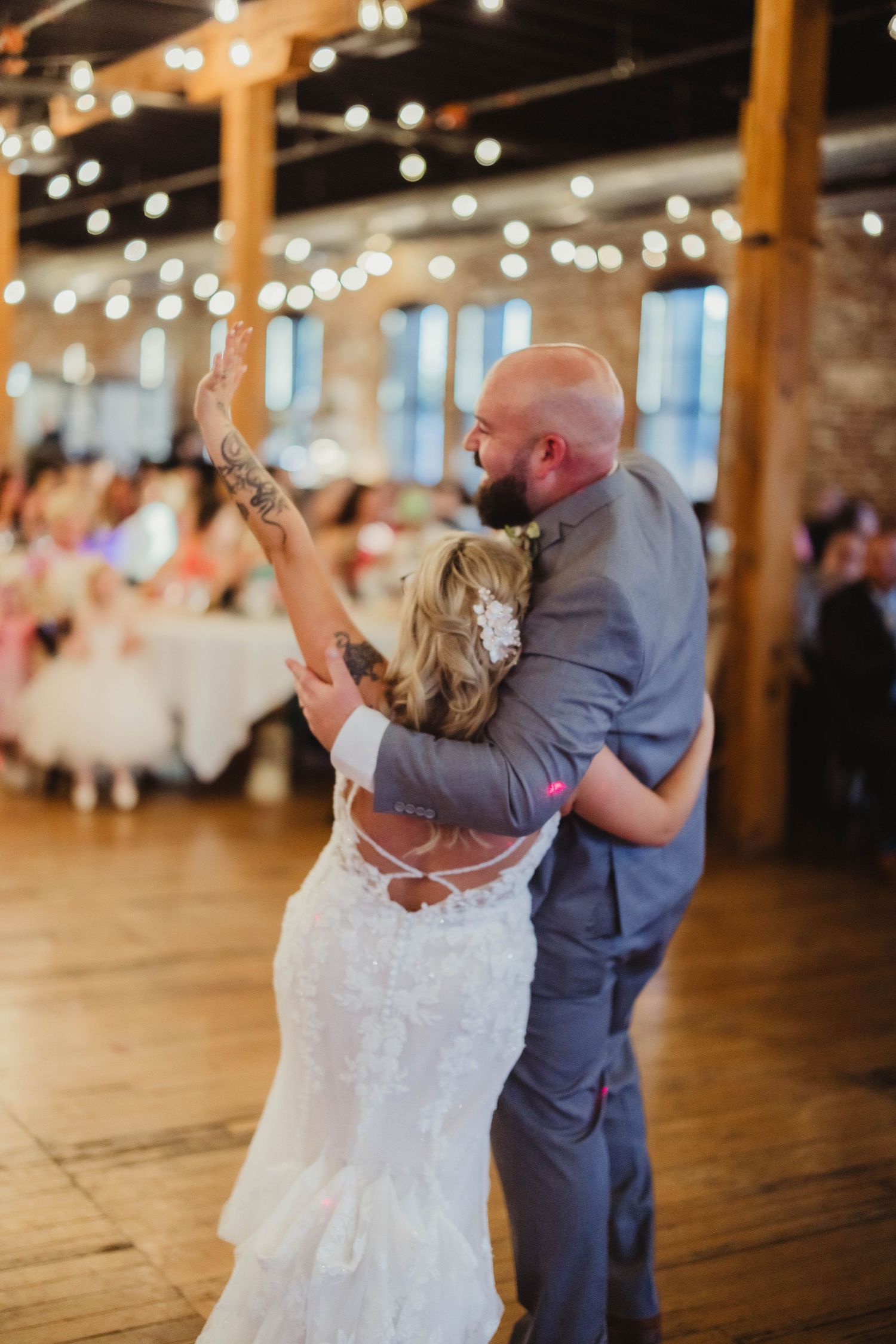 Dancing couple spins under twinkling lights at rustic wedding reception.