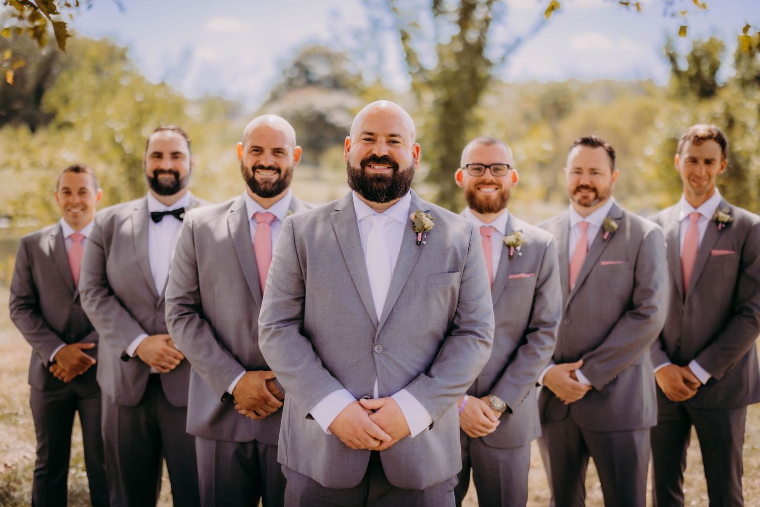 Wedding party members smile while standing in formation wearing coordinated grey suits.