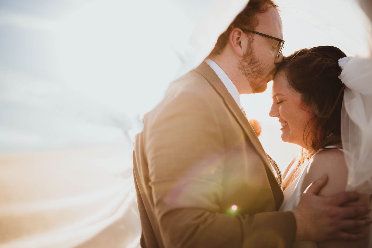 Artistic wedding portrait capturing a gentle kiss between newlyweds in golden sunlight.