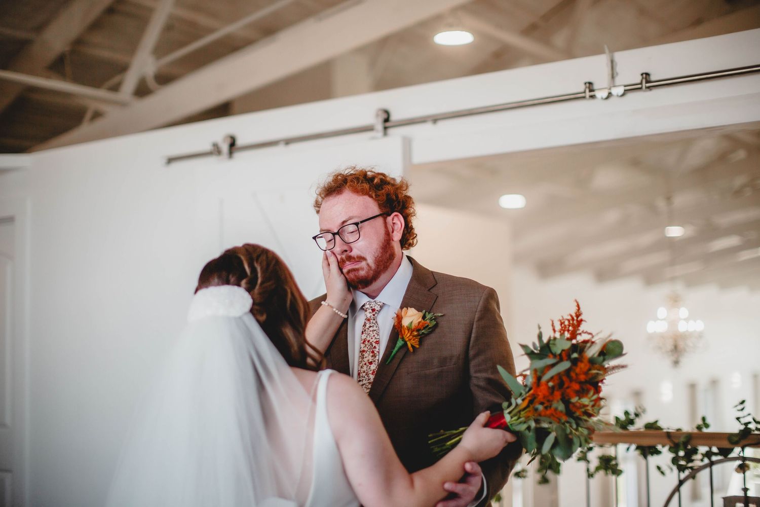 Candid wedding first look moment with brown suit and orange floral bouquet.