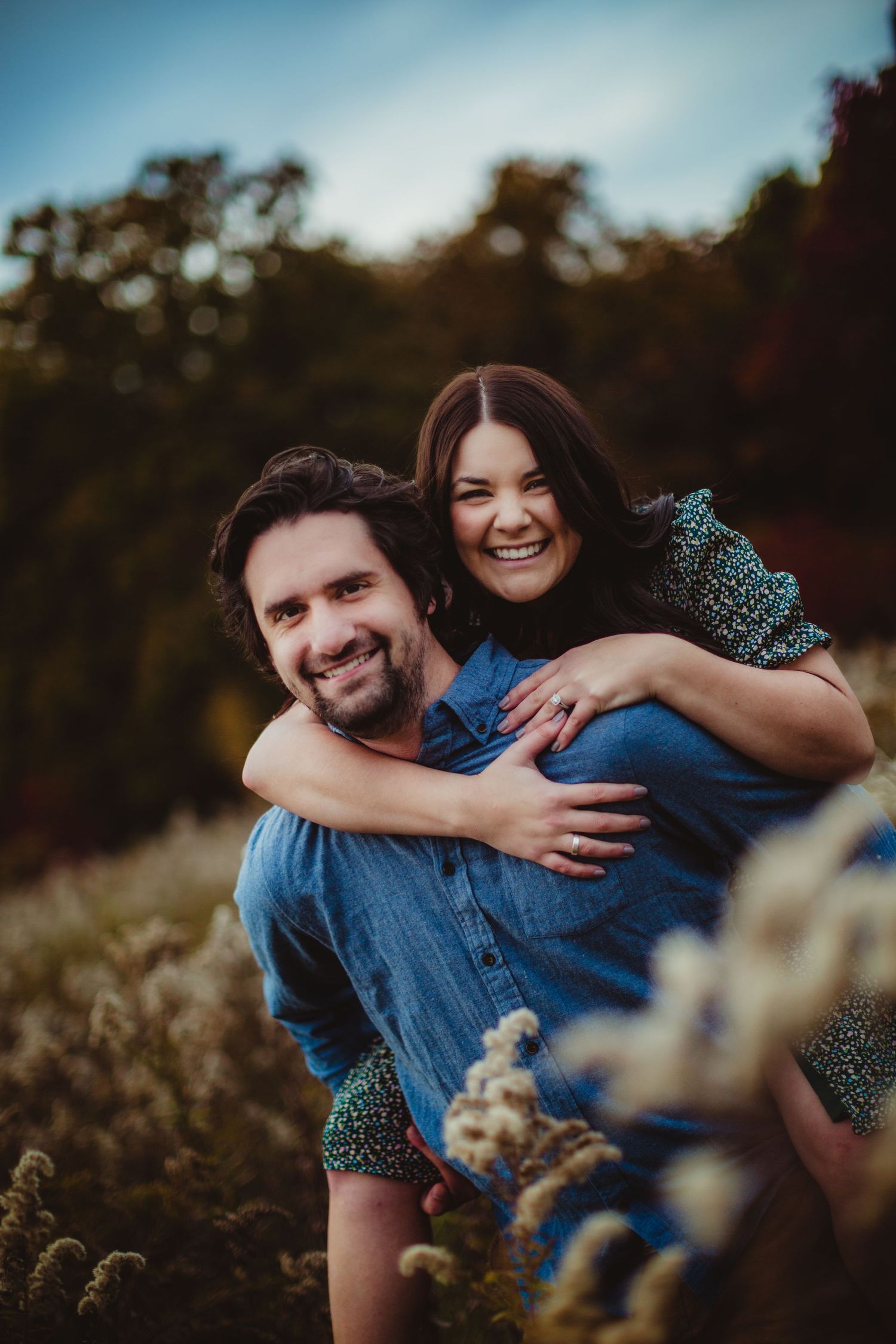 Couple sharing laughter while embracing in a sunlit meadow with wildflowers.