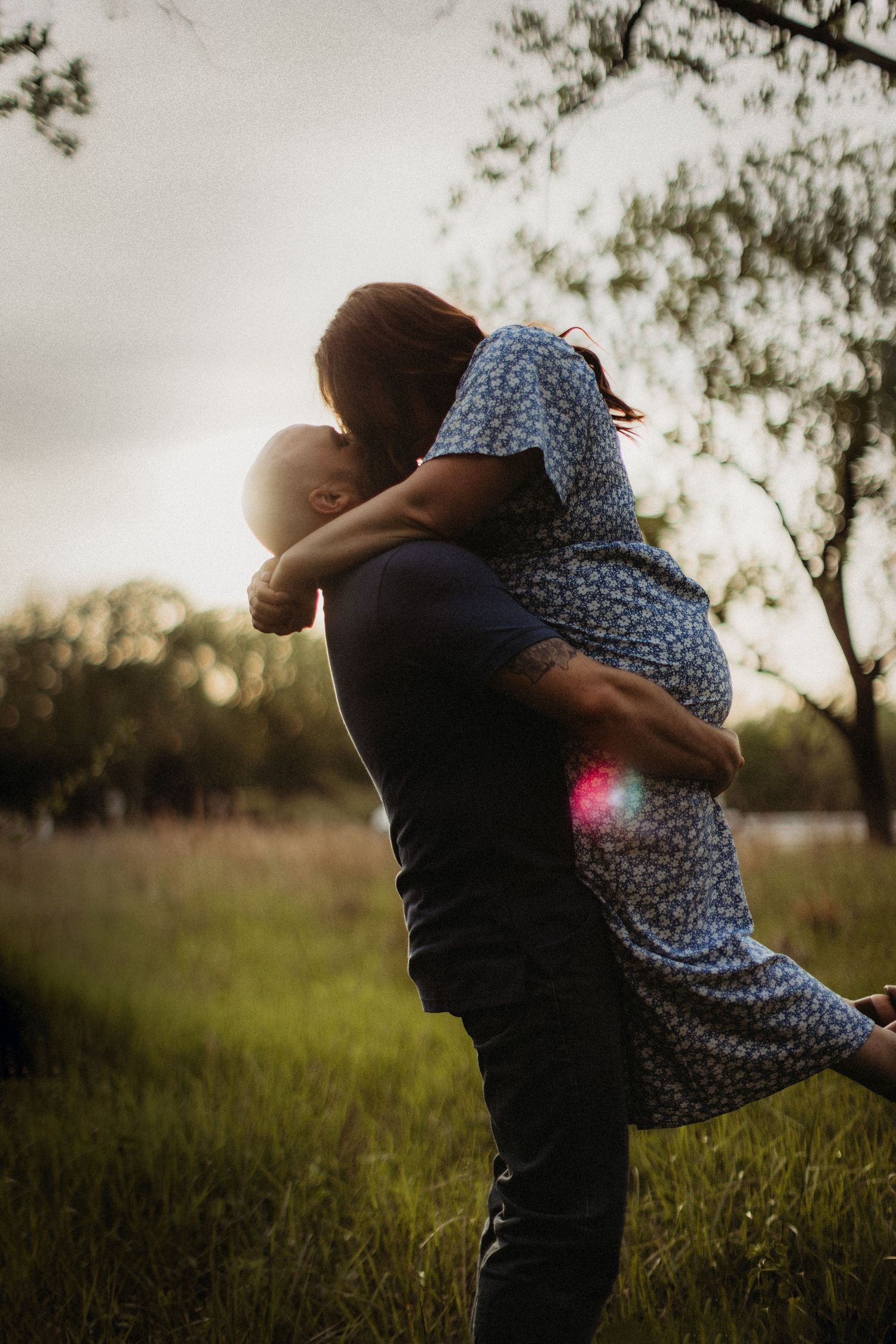 Silhouetted couple sharing an intimate embrace during sunset in a meadow.