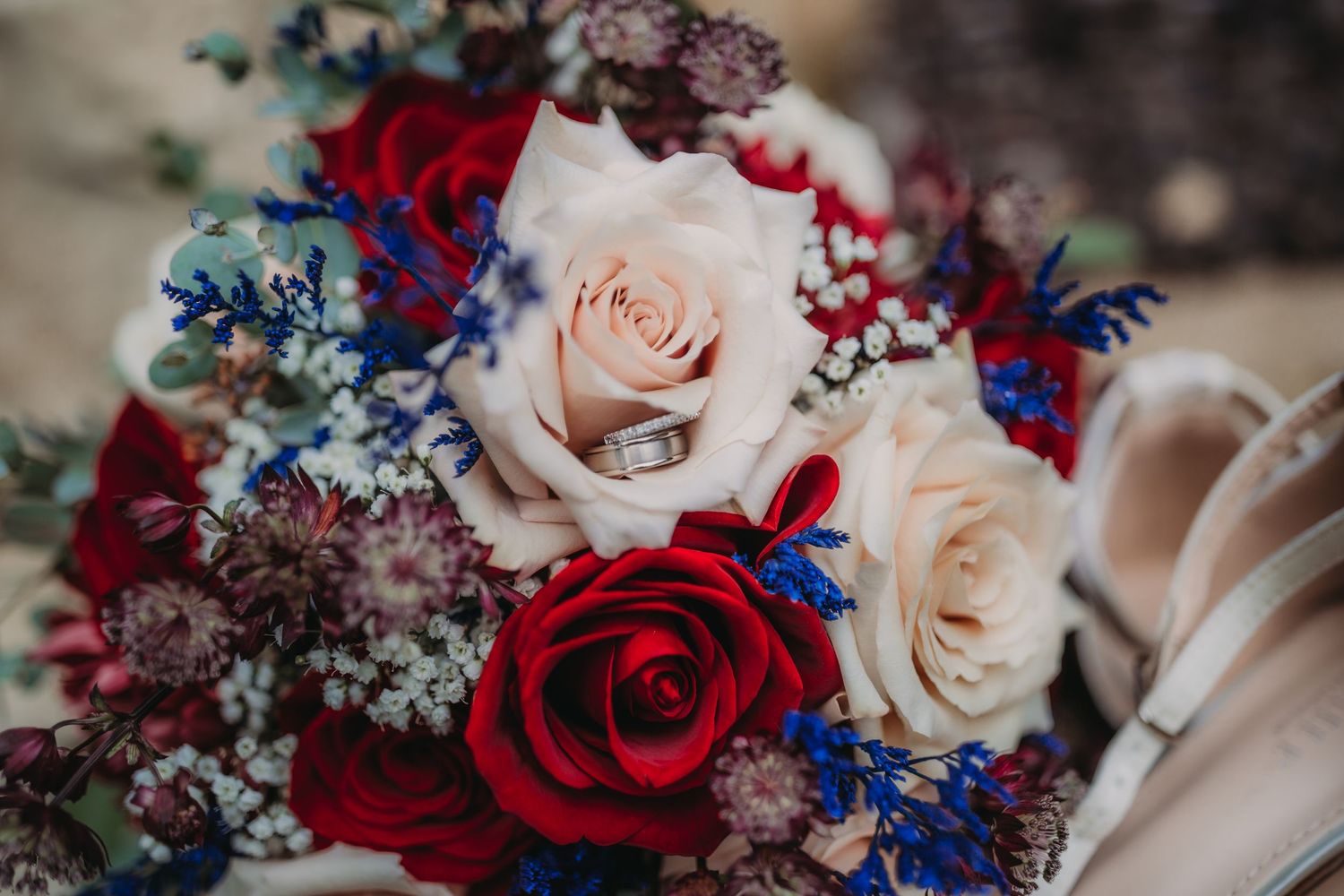 Close-up of wedding bouquet with deep red and pale pink roses accented with blue flowers.