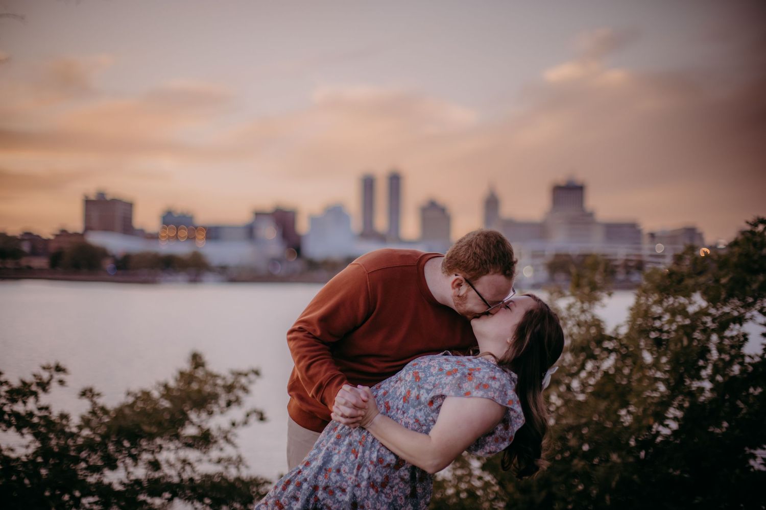 Romantic dip pose silhouetted against city skyline at sunset.