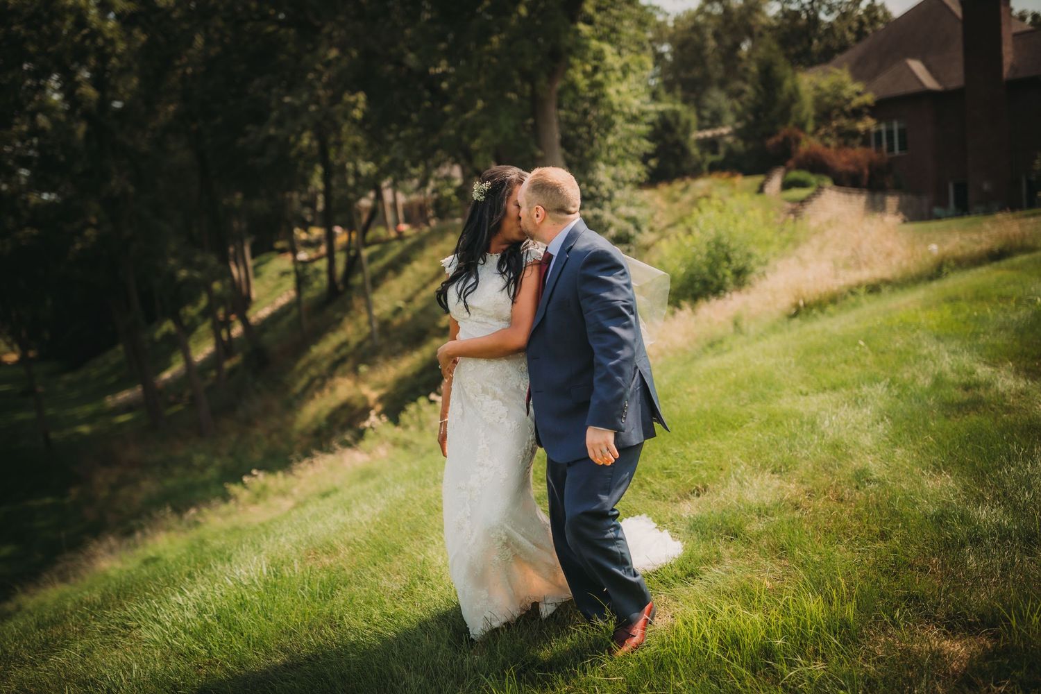 Wedding couple dances together on a sun-dappled grassy hillside.