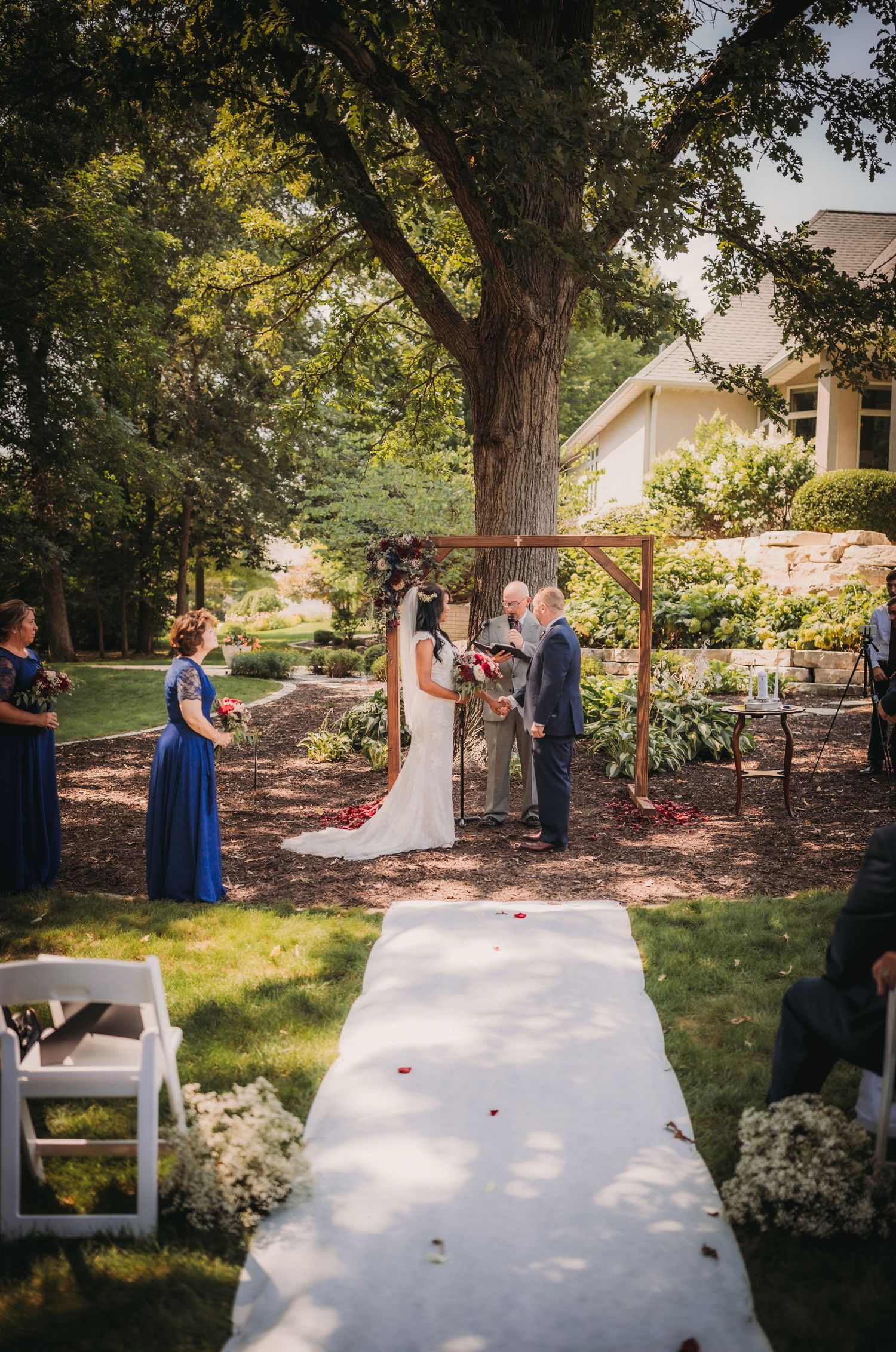 Wedding ceremony space with white aisle runner and wooden chairs in garden setting.