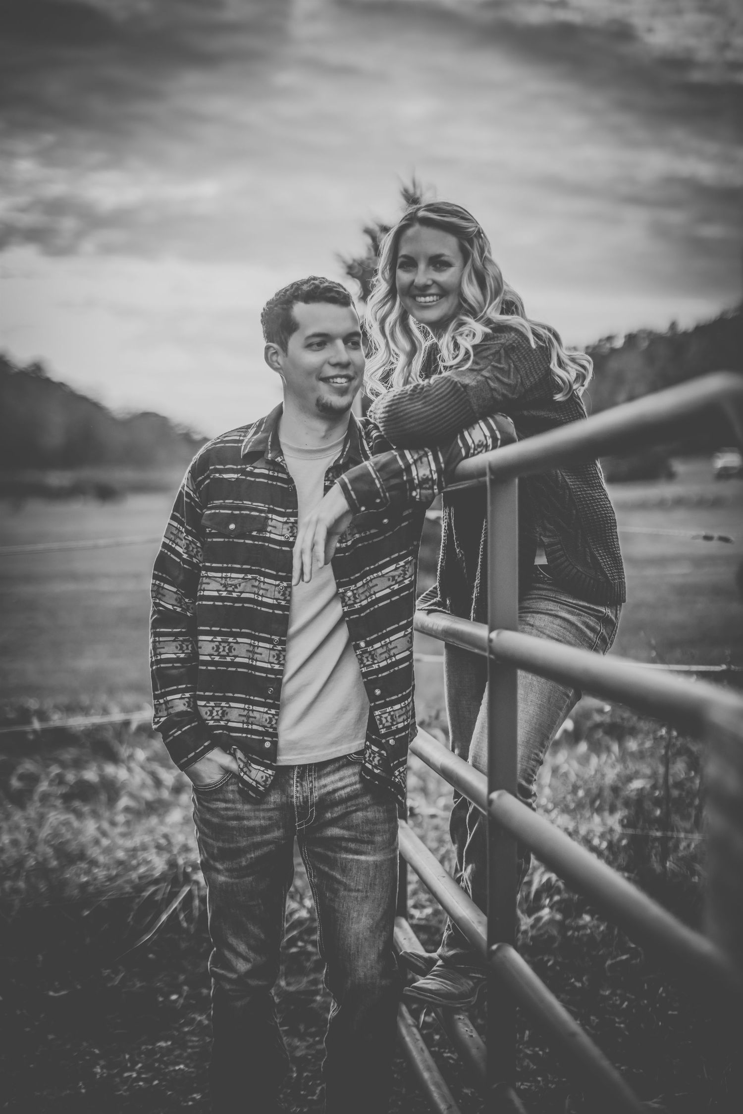 Black and white portrait of couple sharing a moment by wooden fence at dusk.