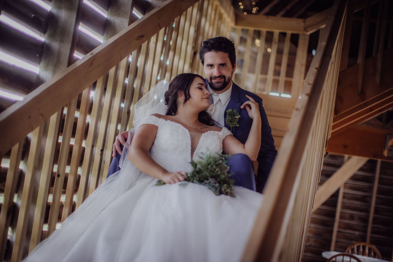 Loving couple shares intimate moment on rustic wooden stairs during wedding celebration.