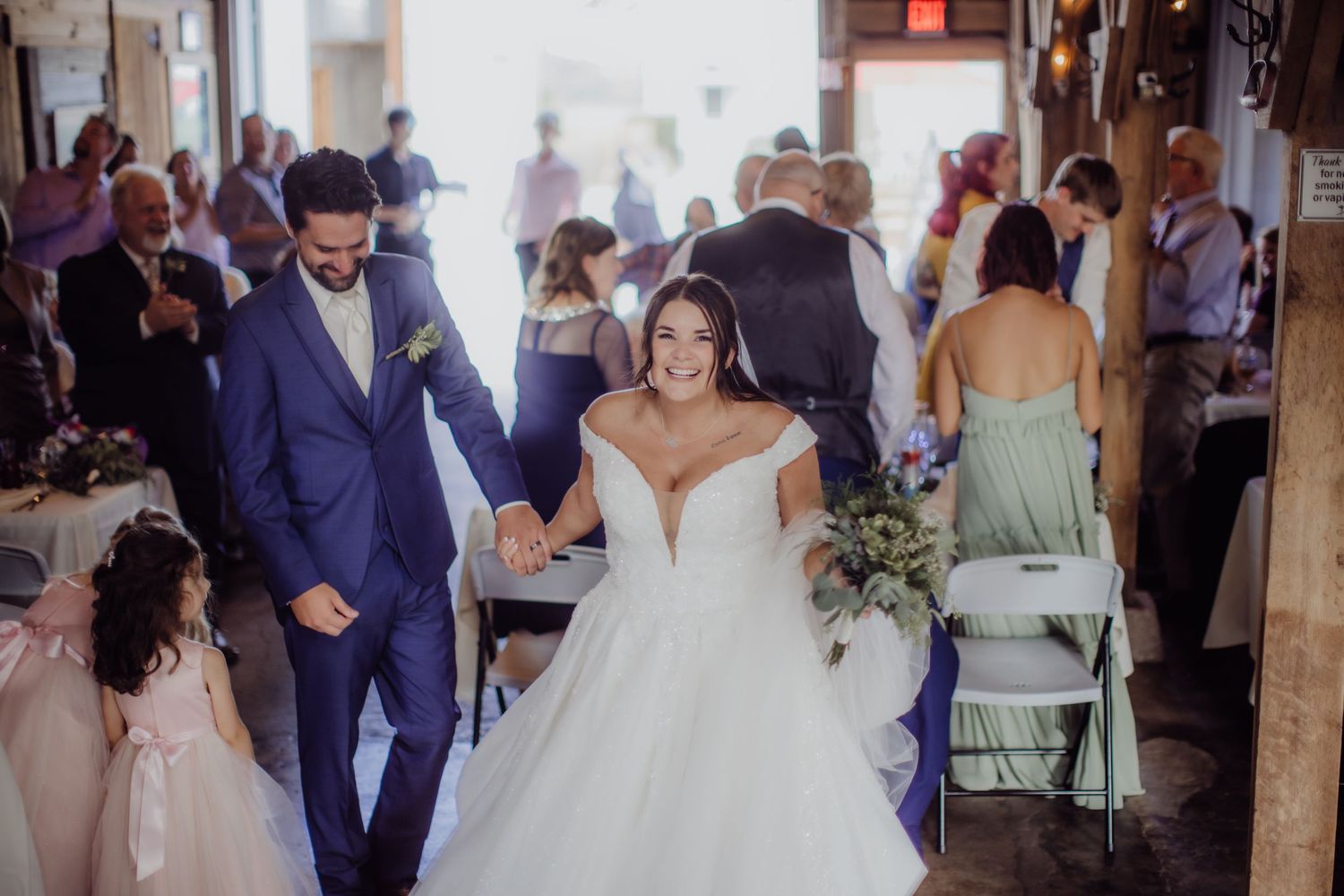 Celebration unfolds as wedding couple walks between rows of seated guests in a rustic venue.