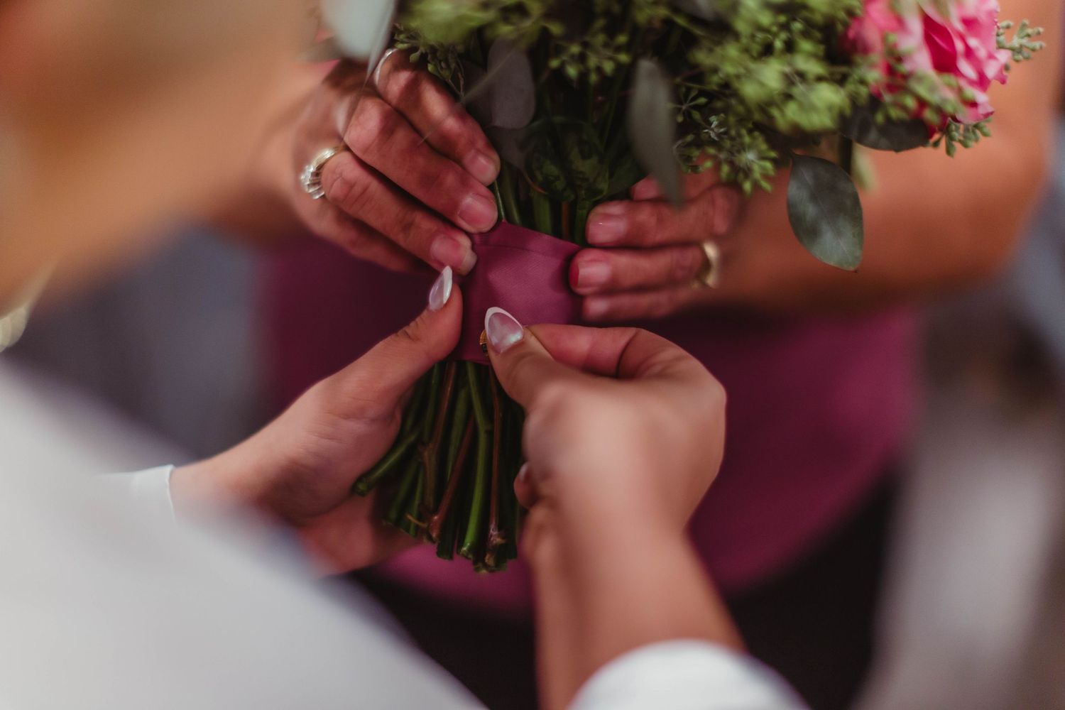 Close-up of hands holding a beautiful pink and green floral wedding bouquet.