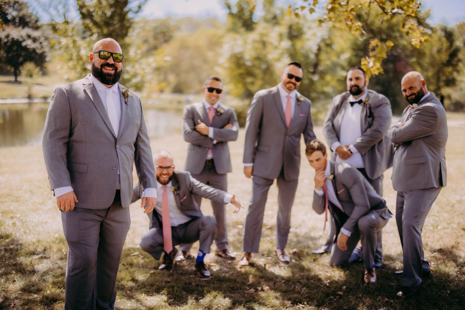 Wedding party members in grey suits playfully posing outdoors.