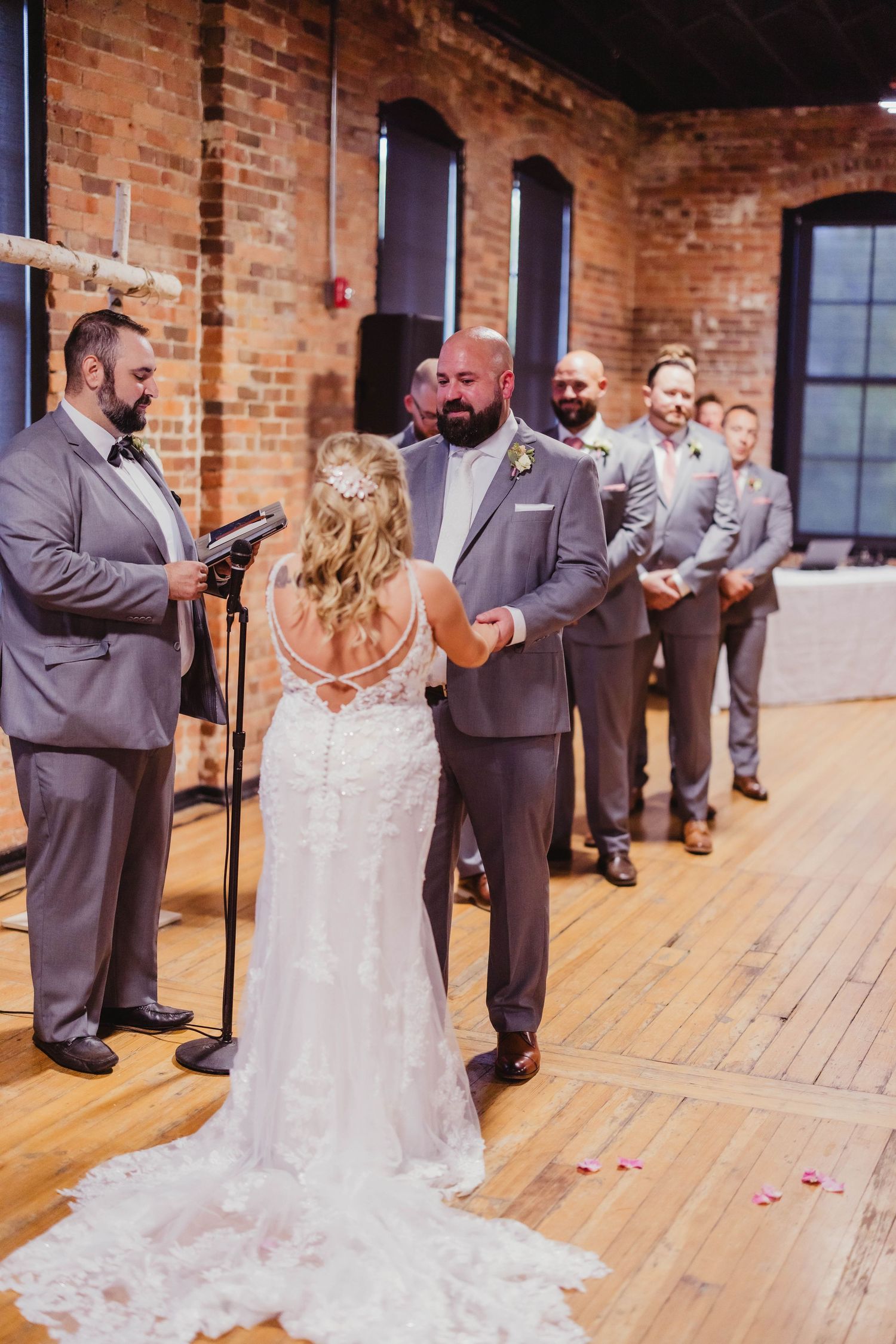 Wedding ceremony in progress on hardwood floors with rustic brick backdrop.