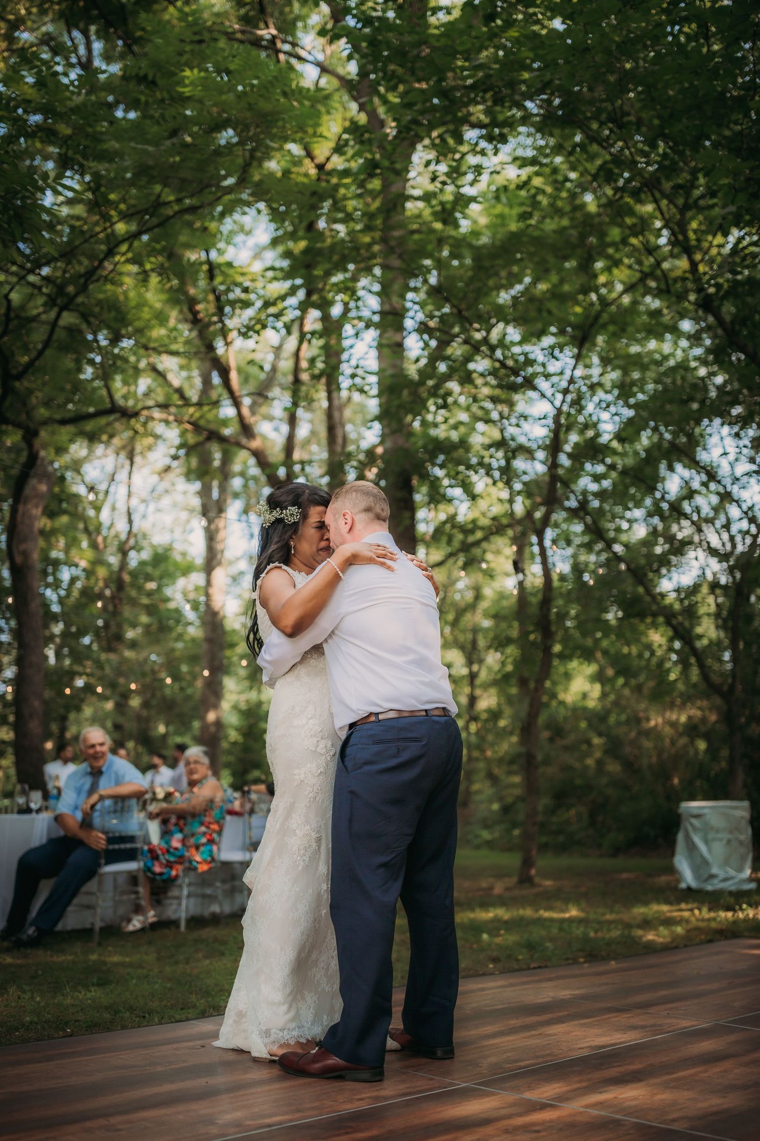 Romantic dance moment captured on an outdoor wooden deck with golden sunlight filtering through the trees.