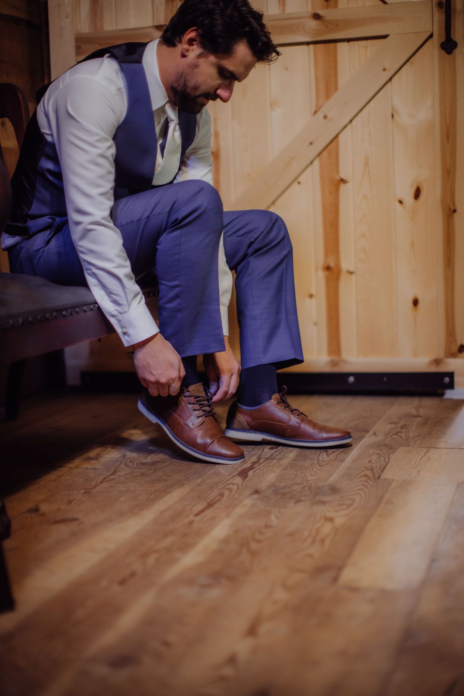 Man in purple suit and white shirt putting on brown leather dress shoes.