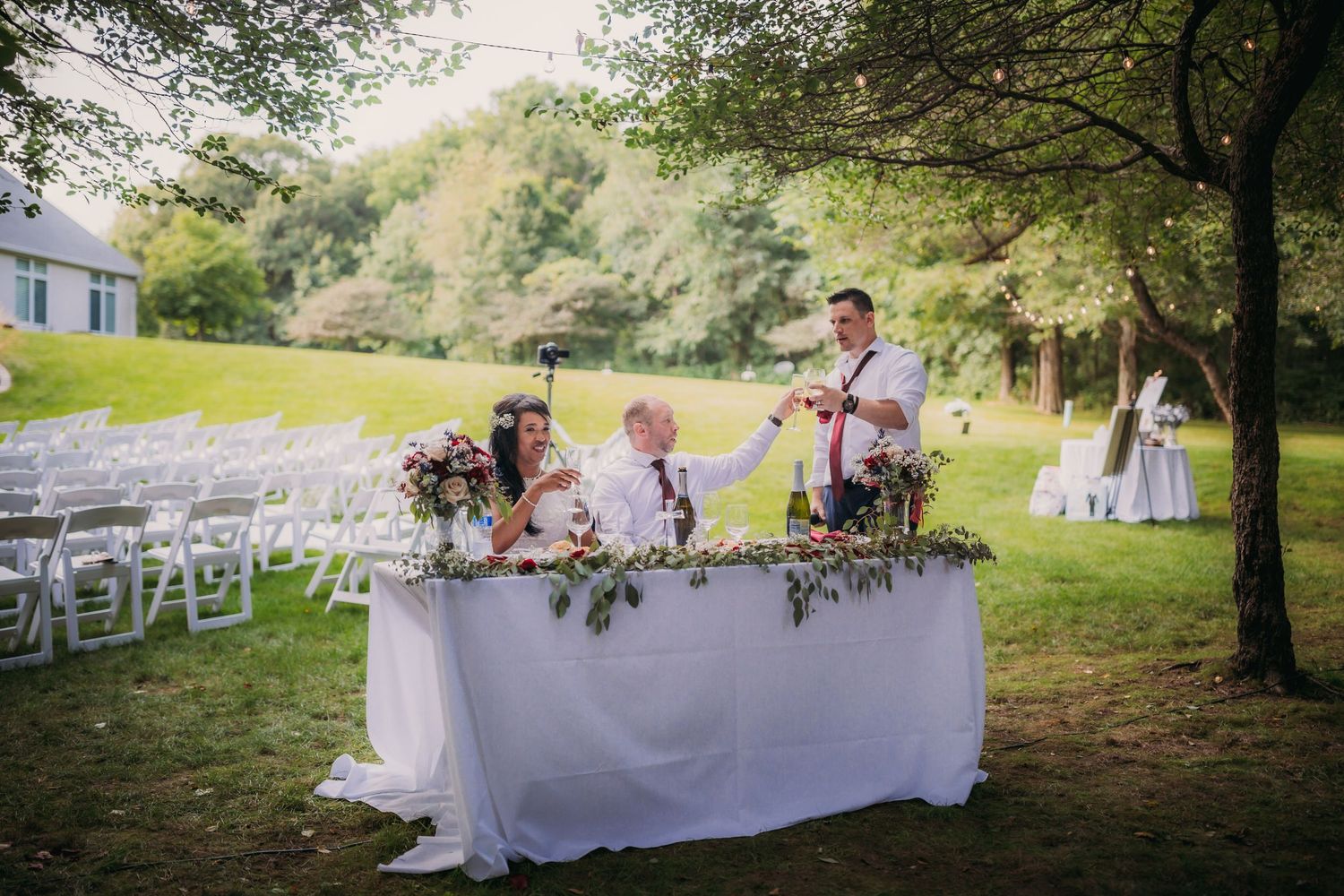 Wedding reception area with elegant white tablecloths and floral arrangements in a natural outdoor setting.