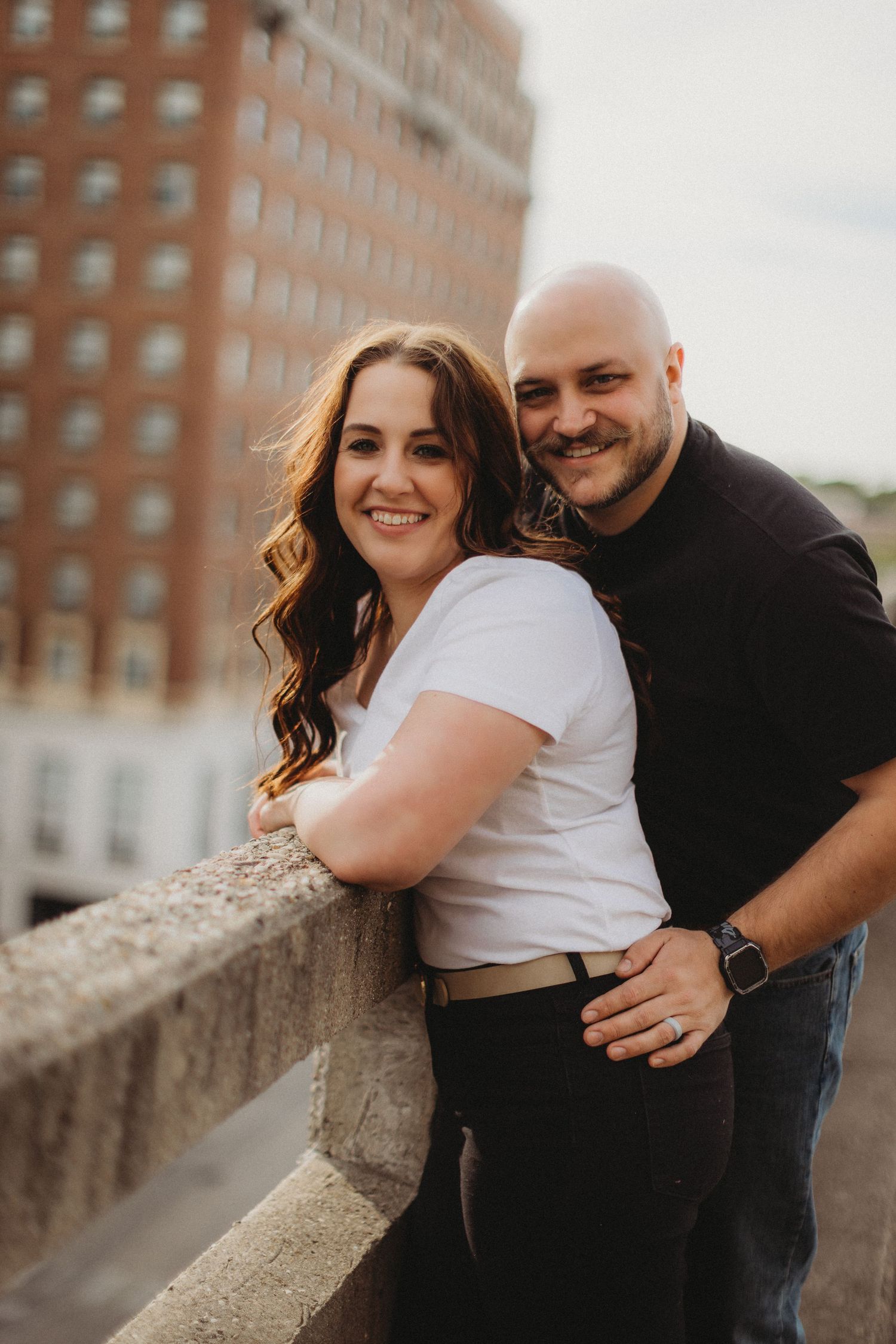 A couple poses together on a rooftop with a historic hotel building visible in the background.