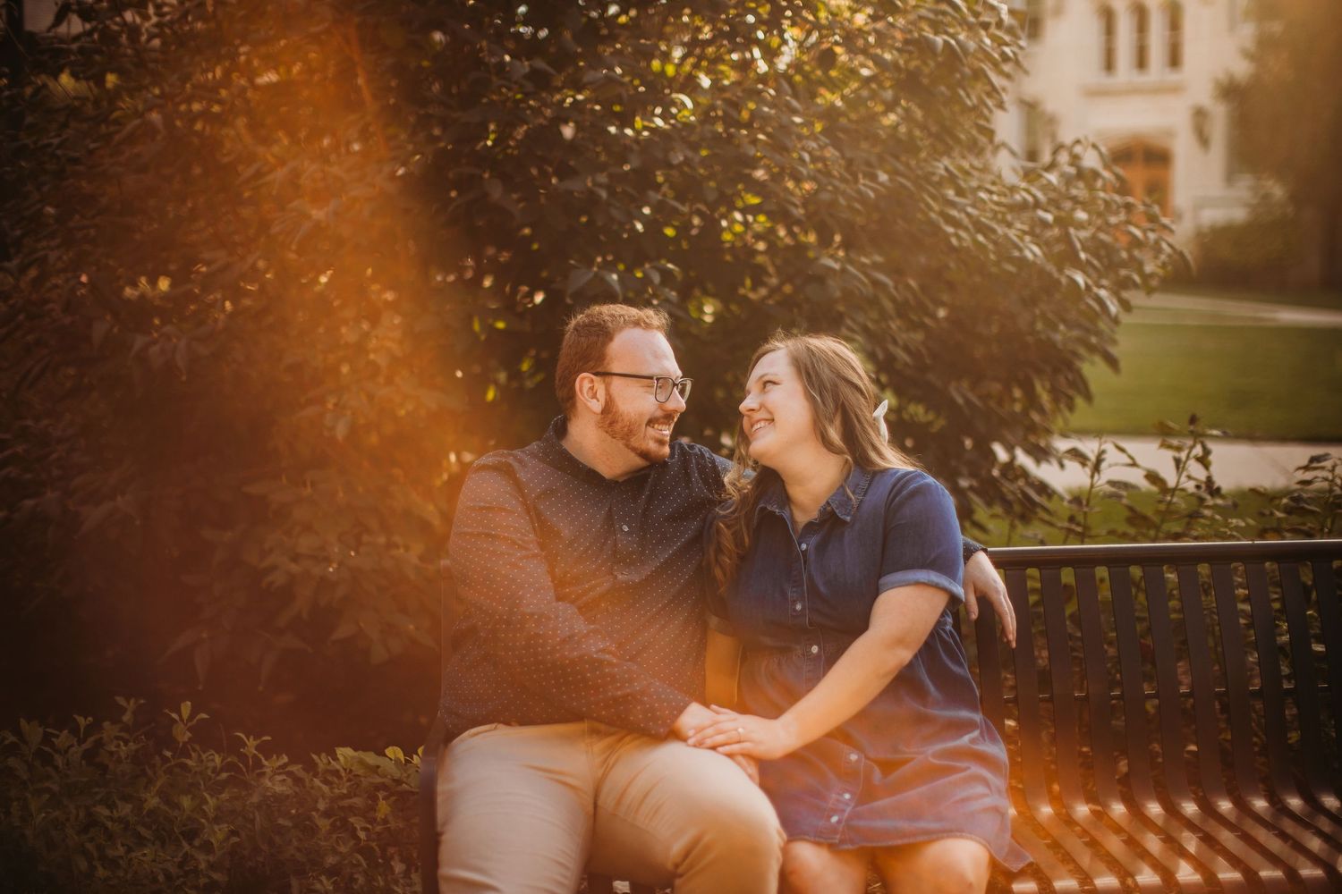 A couple shares a romantic moment on a bench with golden sunlight filtering through trees.