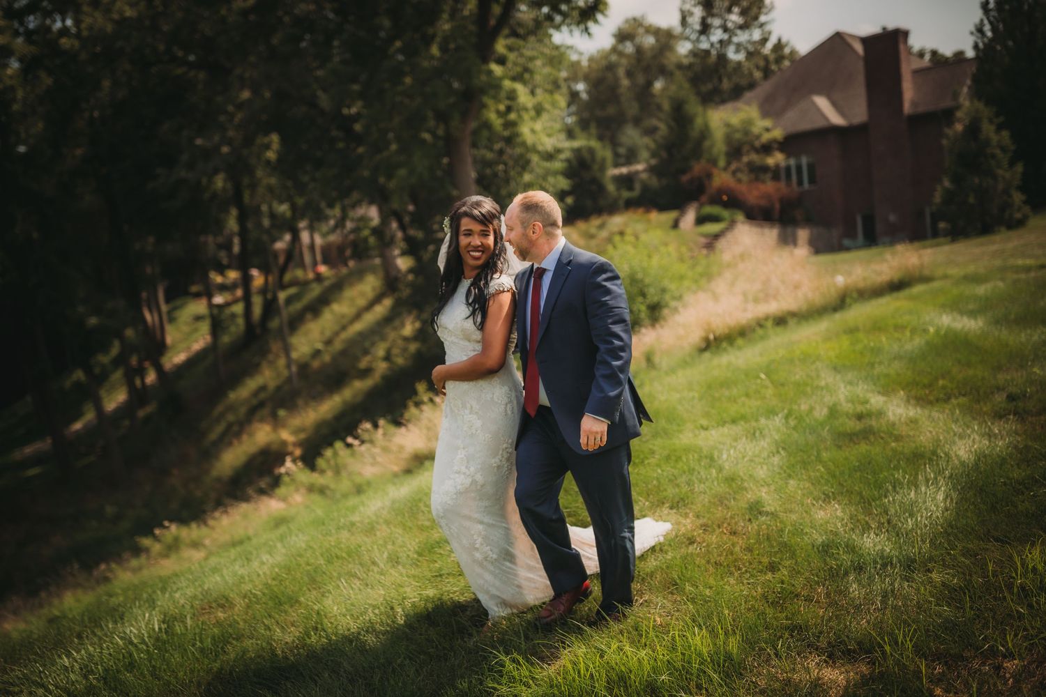 Couple shares a playful moment while walking on a grassy hill during their wedding.