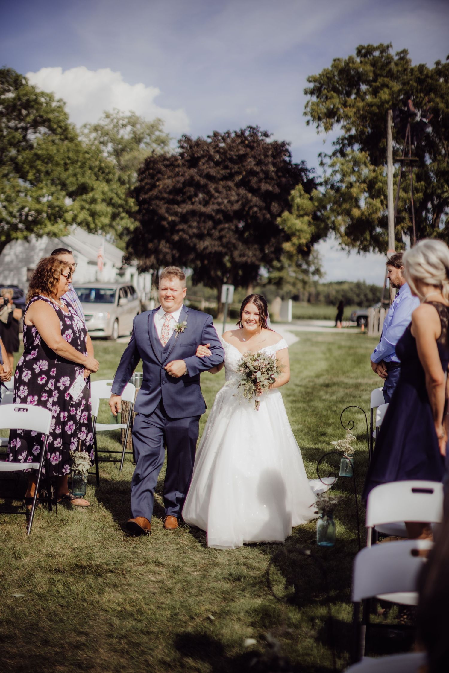 Intimate outdoor wedding ceremony taking place on grassy lawn with trees in background.