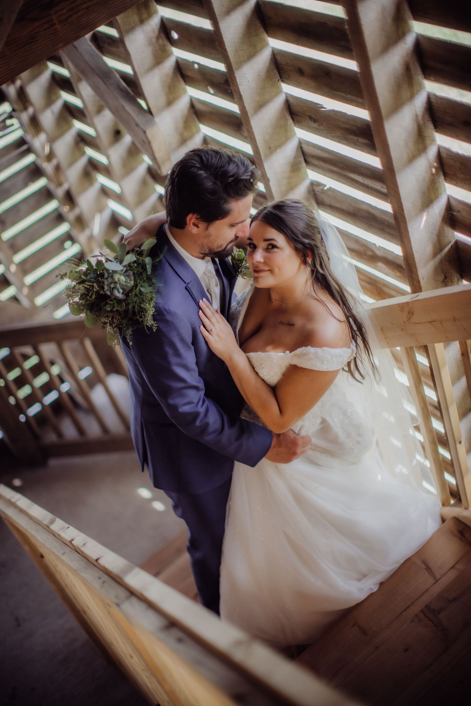 Intimate wedding moment captured on rustic wooden stairs with sunlit geometric shadows.