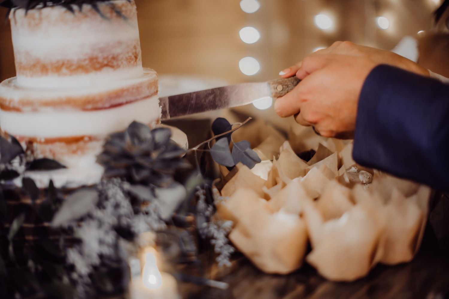 Close-up shot of hands cutting into an elegant tiered white wedding cake.