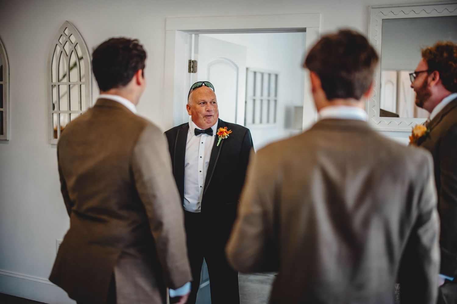 Wedding party members in suits gather in a bright room while getting ready.