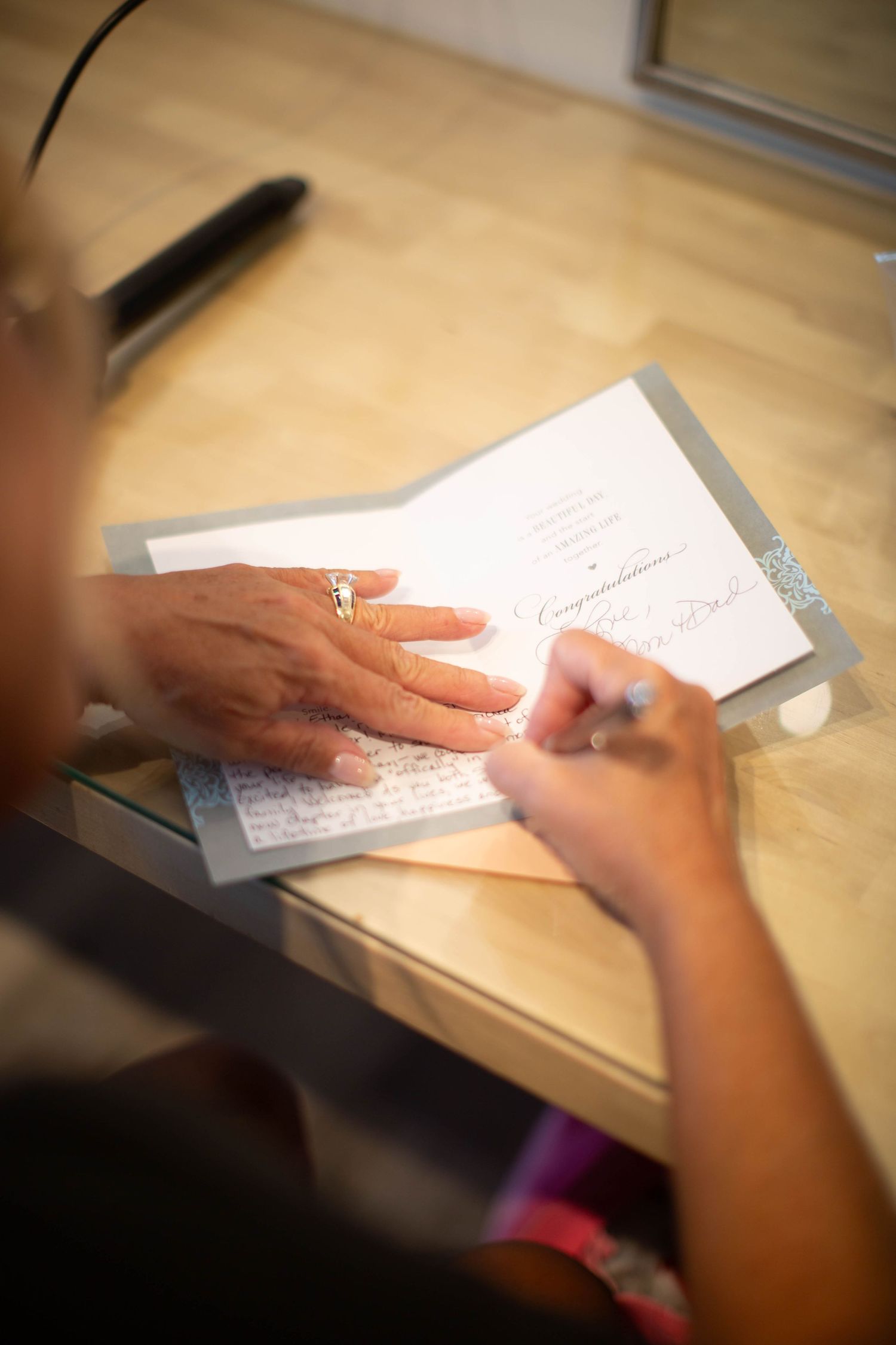 Close-up of hands writing on paper, signing what appears to be a document or card.