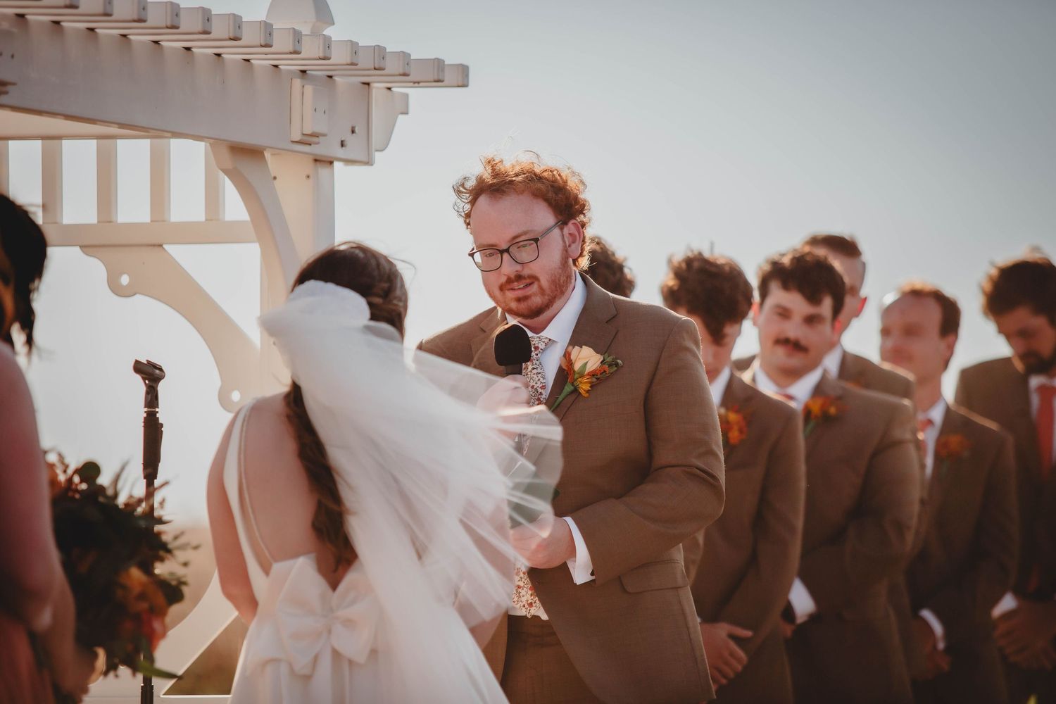 Outdoor wedding ceremony with couple exchanging vows under white pergola.