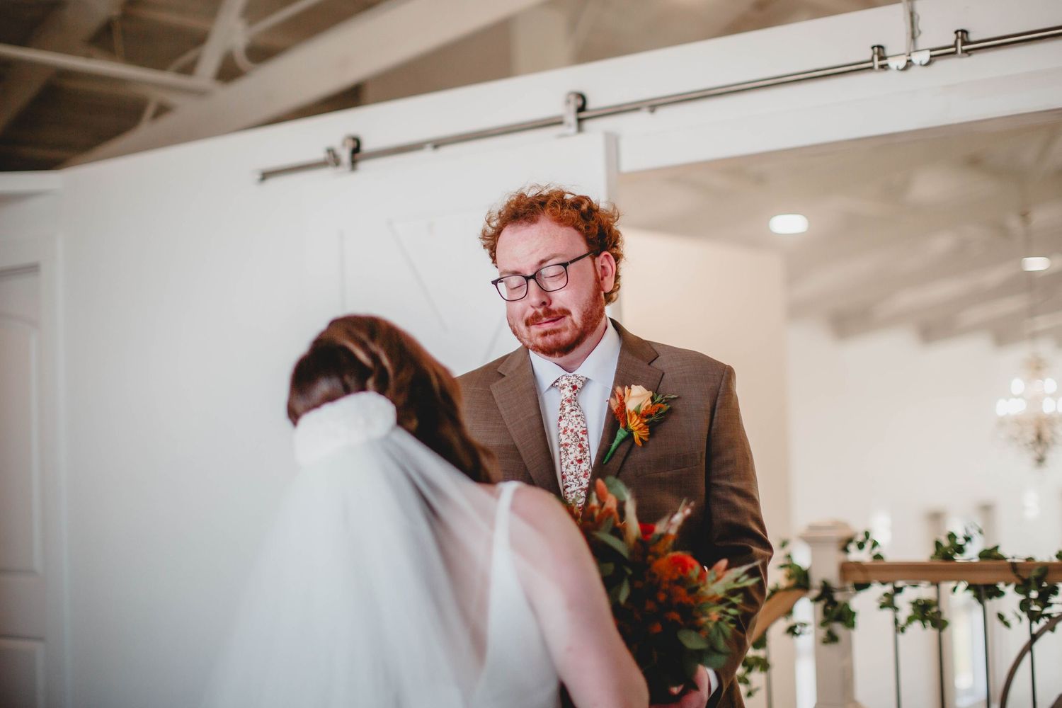 Wedding couple shares an intimate first look moment in a light-filled venue with fall-colored floral bouquet.