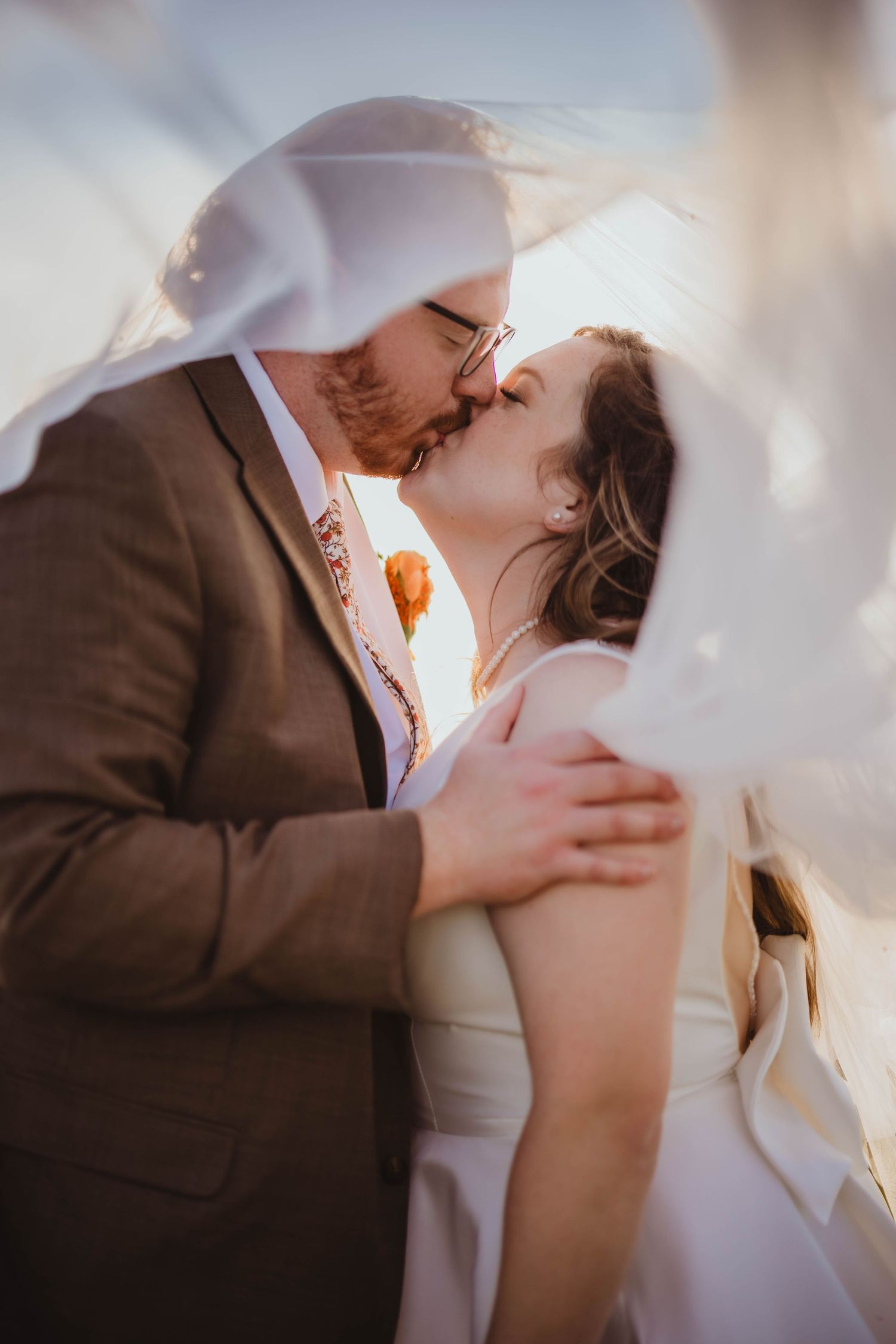 A romantic wedding moment with a white veil flowing in the breeze as a couple shares a tender kiss.