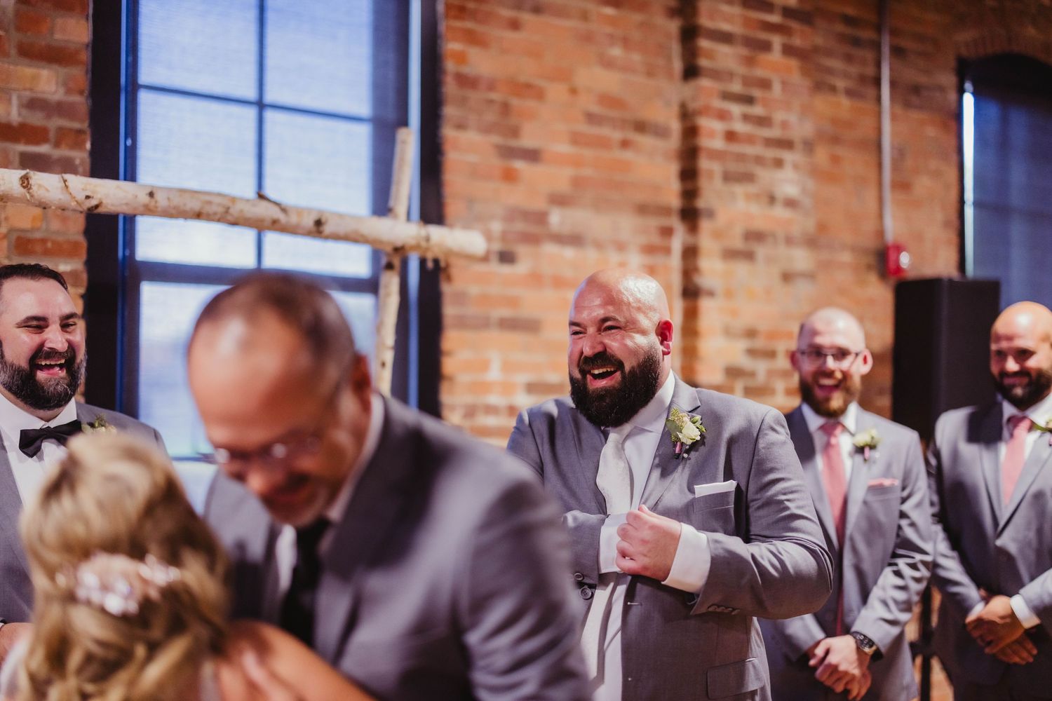 Wedding ceremony participants react with joy in rustic brick-walled venue.