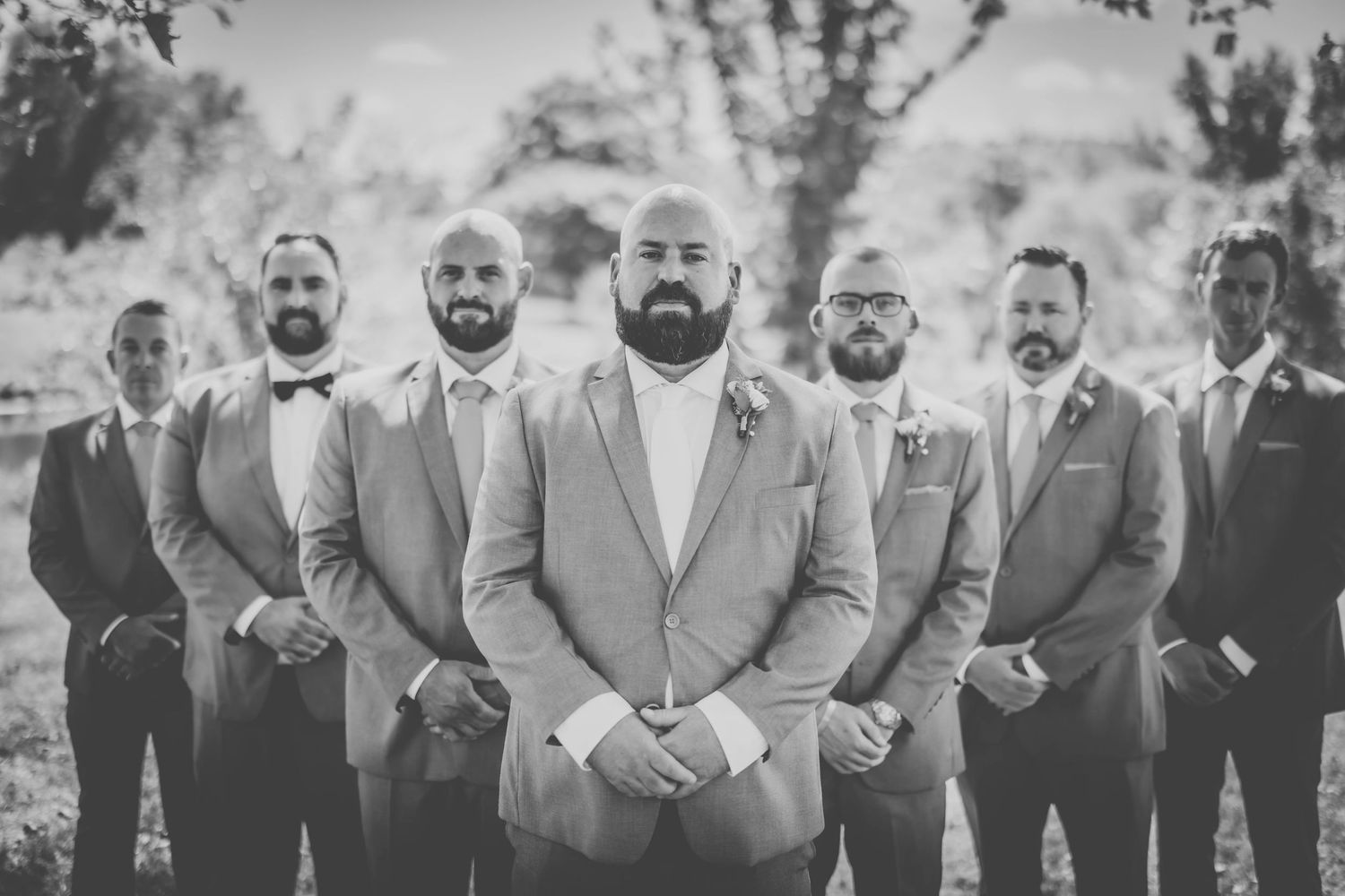 Black and white photo of wedding party members posing in grey suits outdoors.