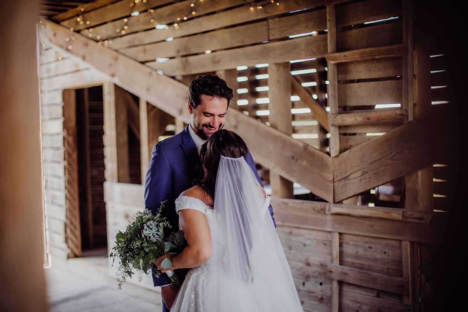 First look wedding photos showing tender moments in a barn with string lights.