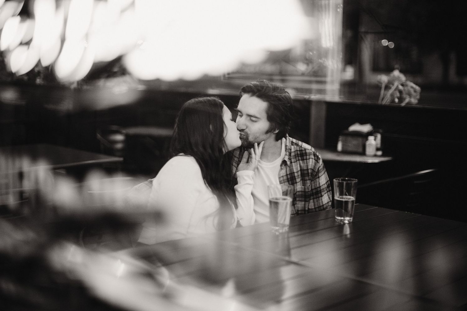 Black and white photo of a couple sharing an intimate moment in a moody bar setting.