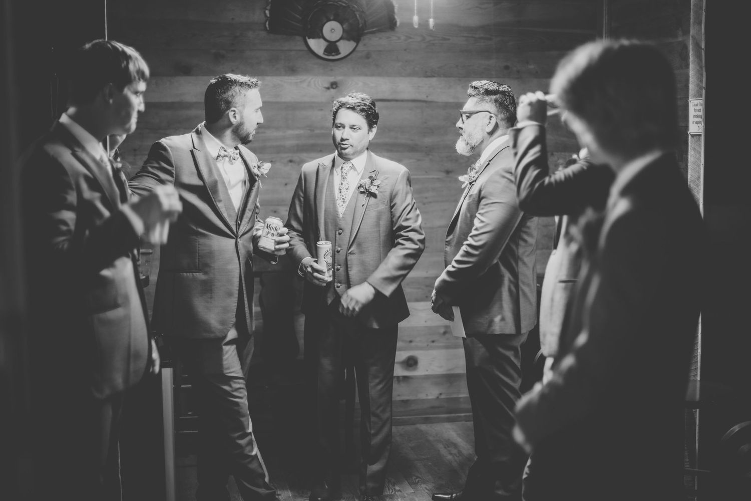 Black and white photo of groomsmen gathered in rustic indoor setting.