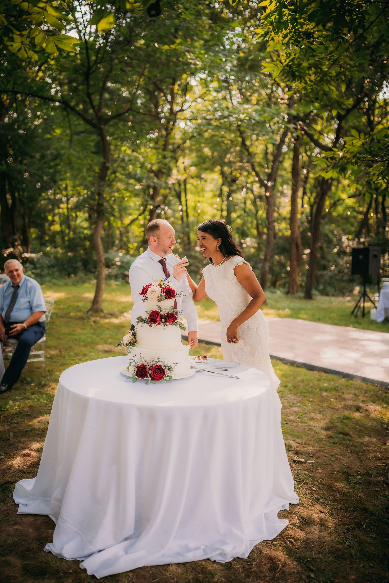 Wedding couple at round table during golden hour with elegant white cake and floral decorations.