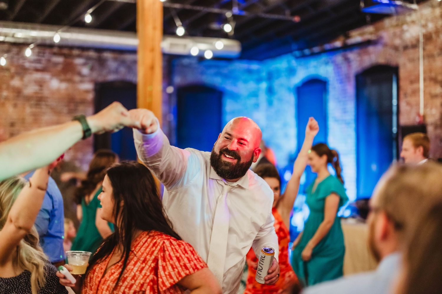 Dancers celebrate at a lively indoor reception with exposed brick walls and blue lighting in the background.