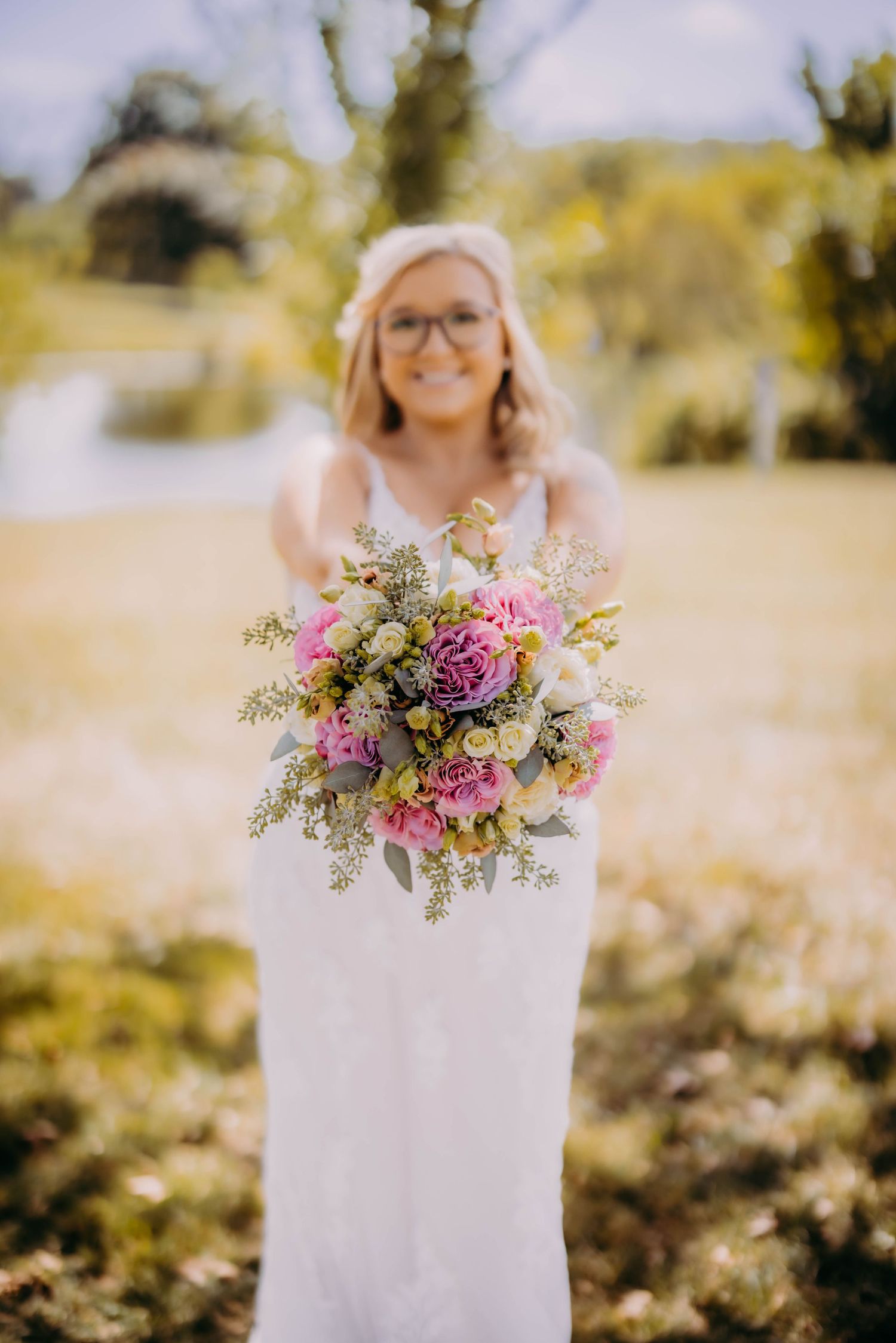 Wedding dress and bouquet details against sunlit natural outdoor background.