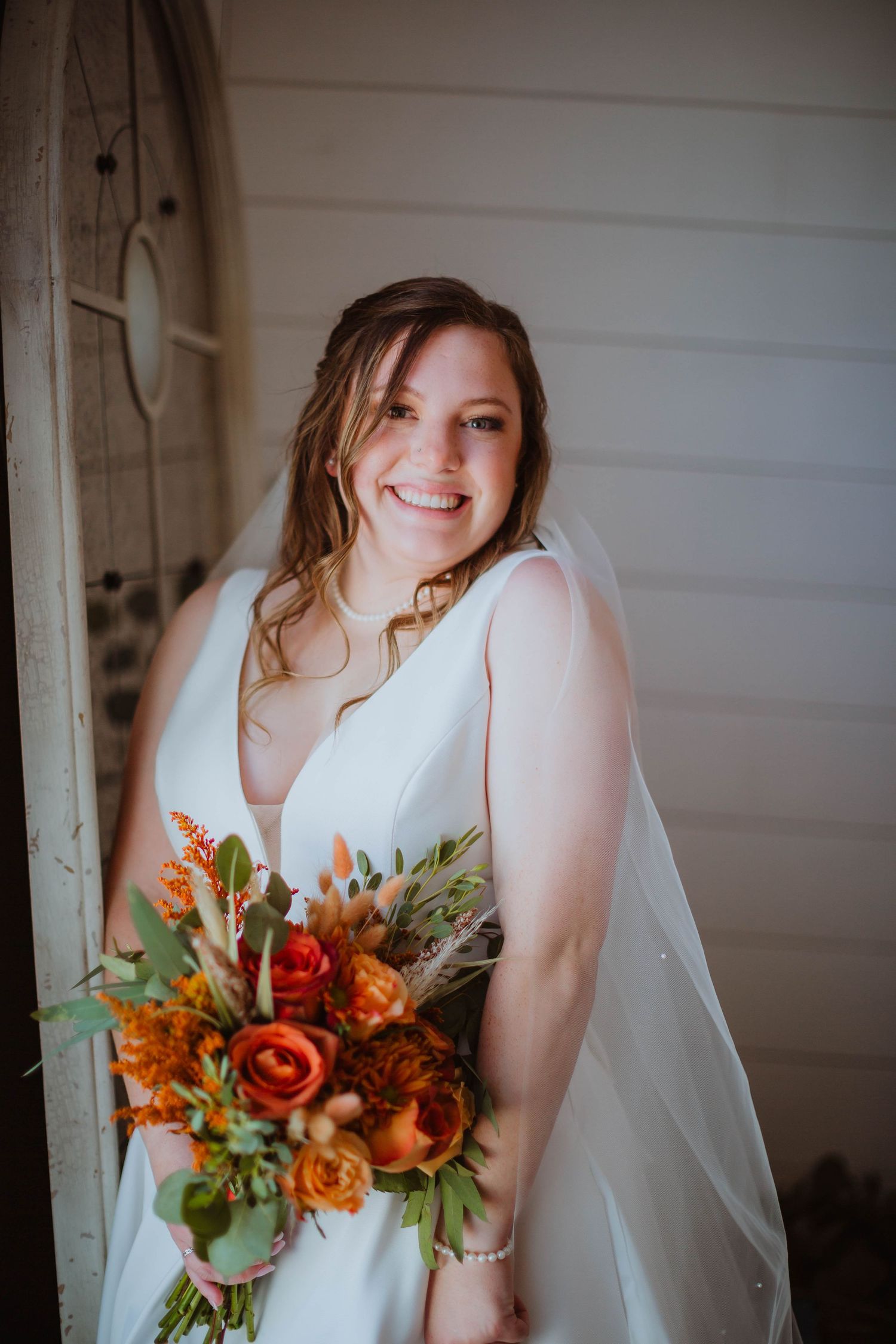 A bride holds a vibrant orange and red fall bouquet while wearing a classic white gown.