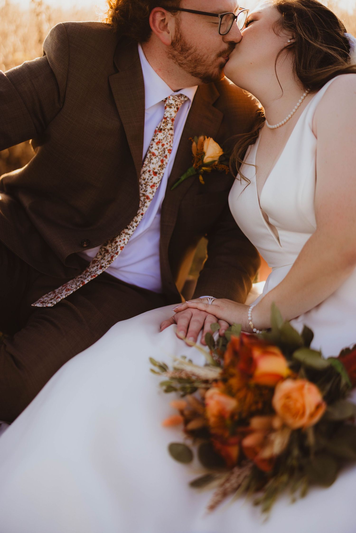 Wedding couple embracing with orange floral bouquet details against warm autumn backdrop.