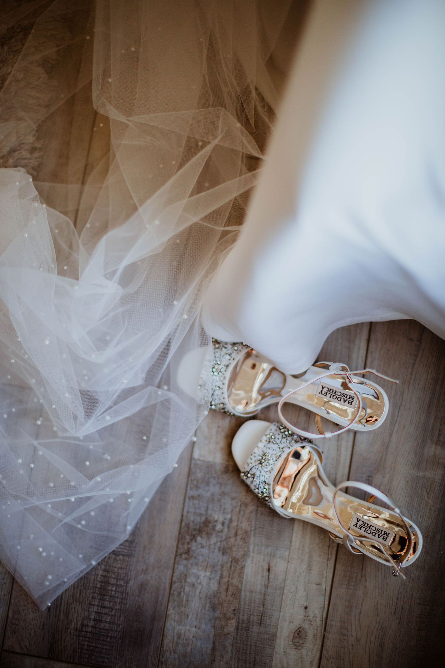 Wedding shoes and delicate tulle veil arranged on rustic wooden floor.