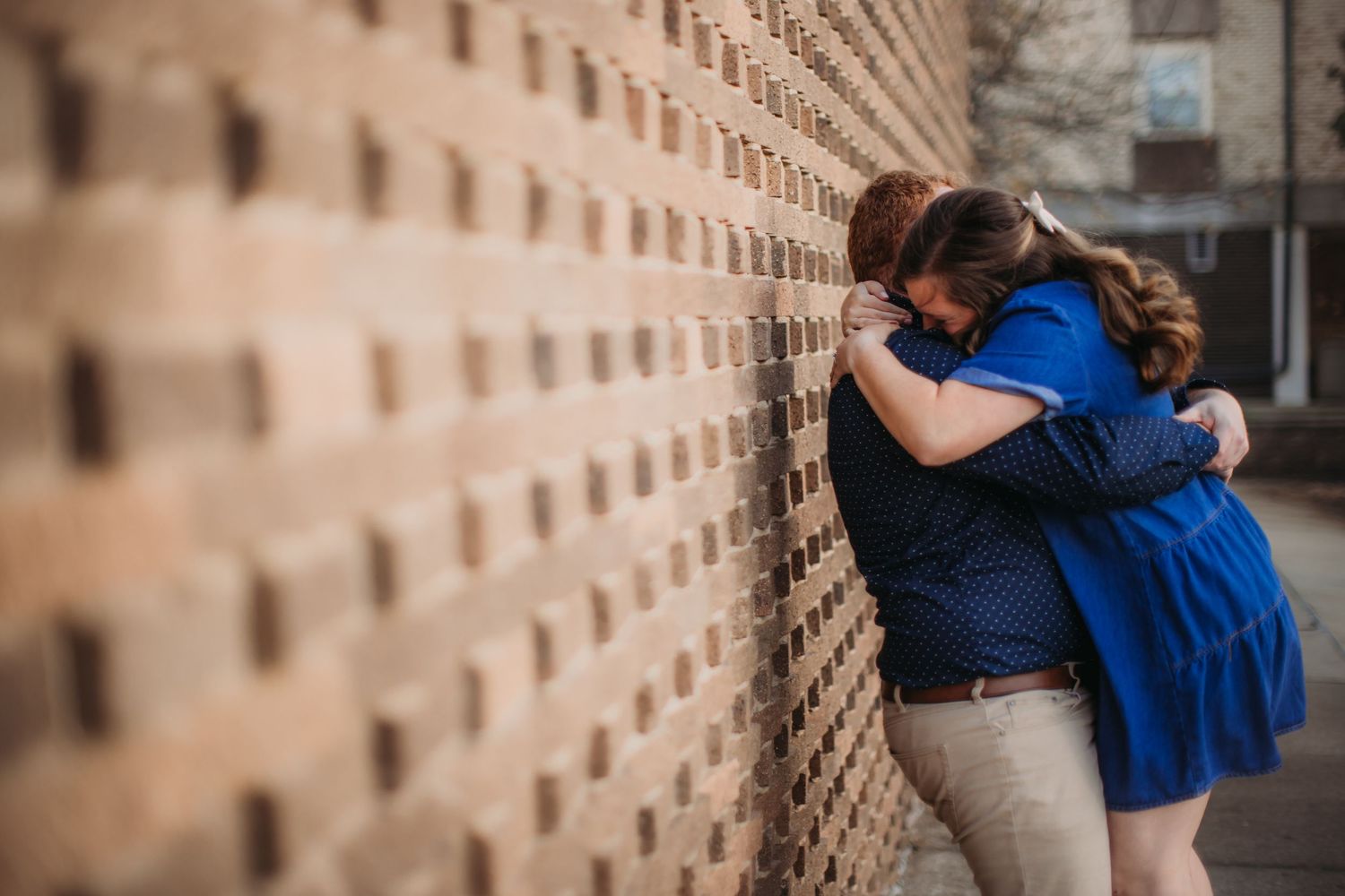 A joyful embrace captured in front of a geometric patterned brick wall.