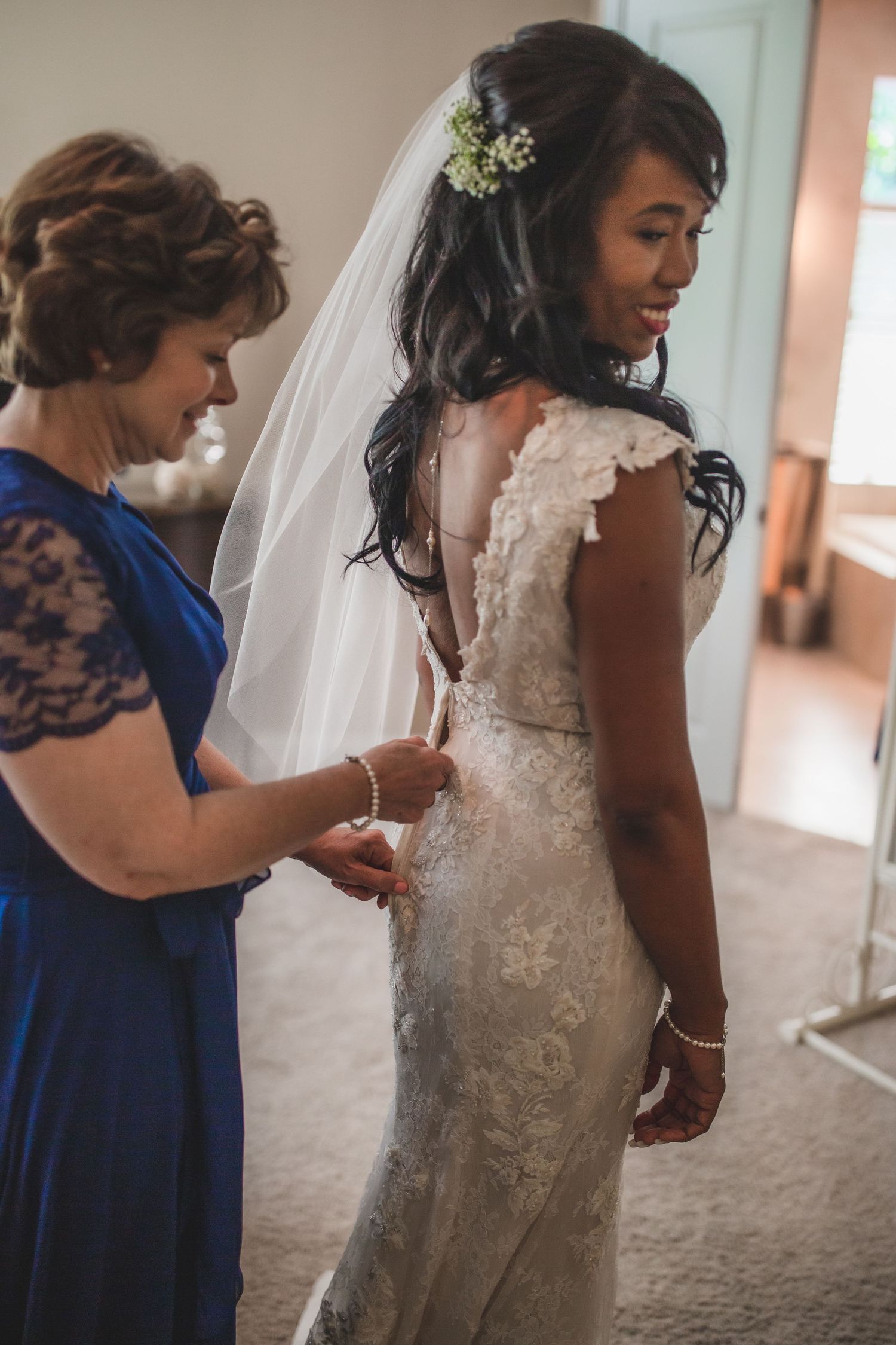 Back view of lace wedding dress being adjusted during bridal preparations.
