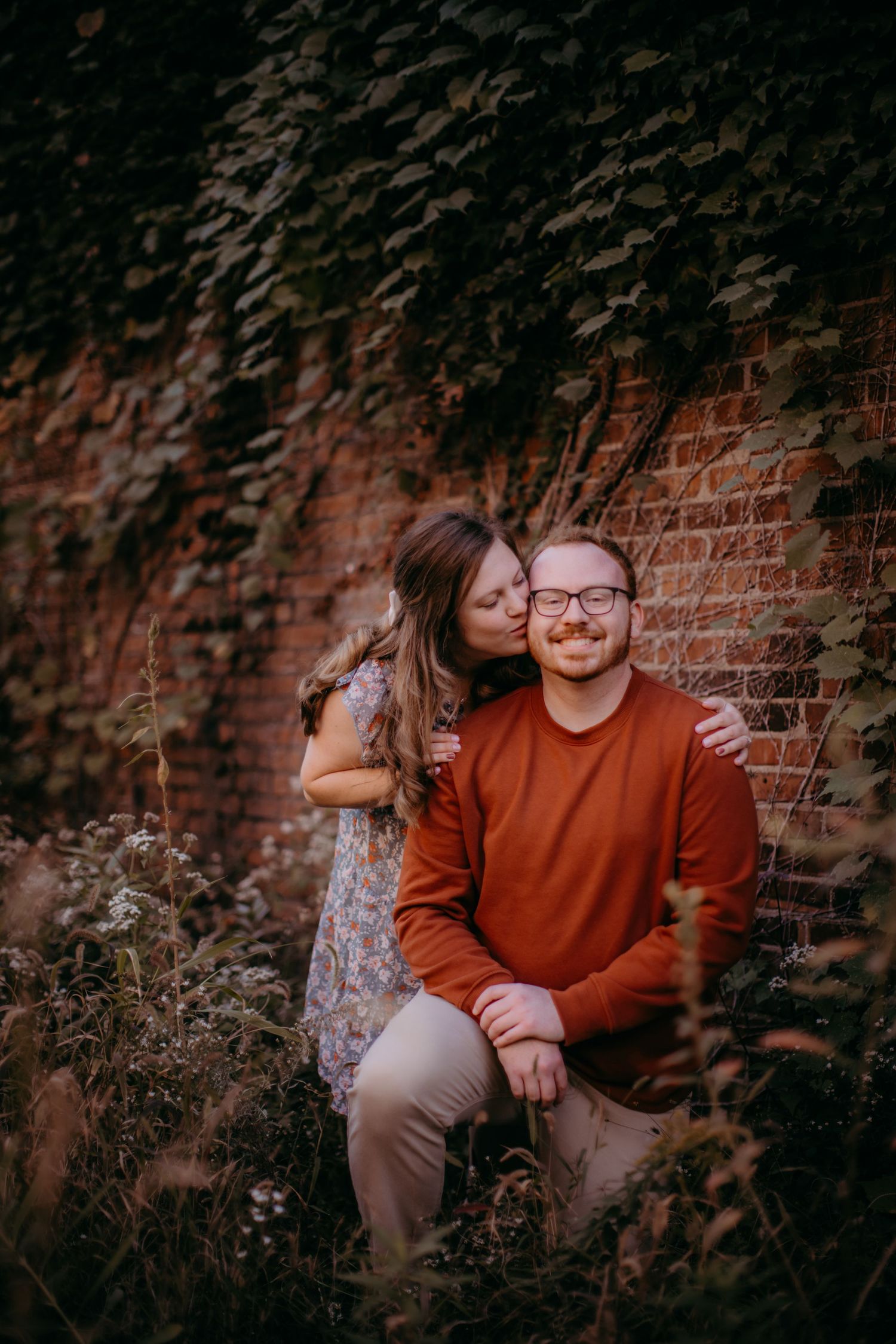 A couple shares a tender moment against a rustic brick wall background in a romantic outdoor photoshoot.