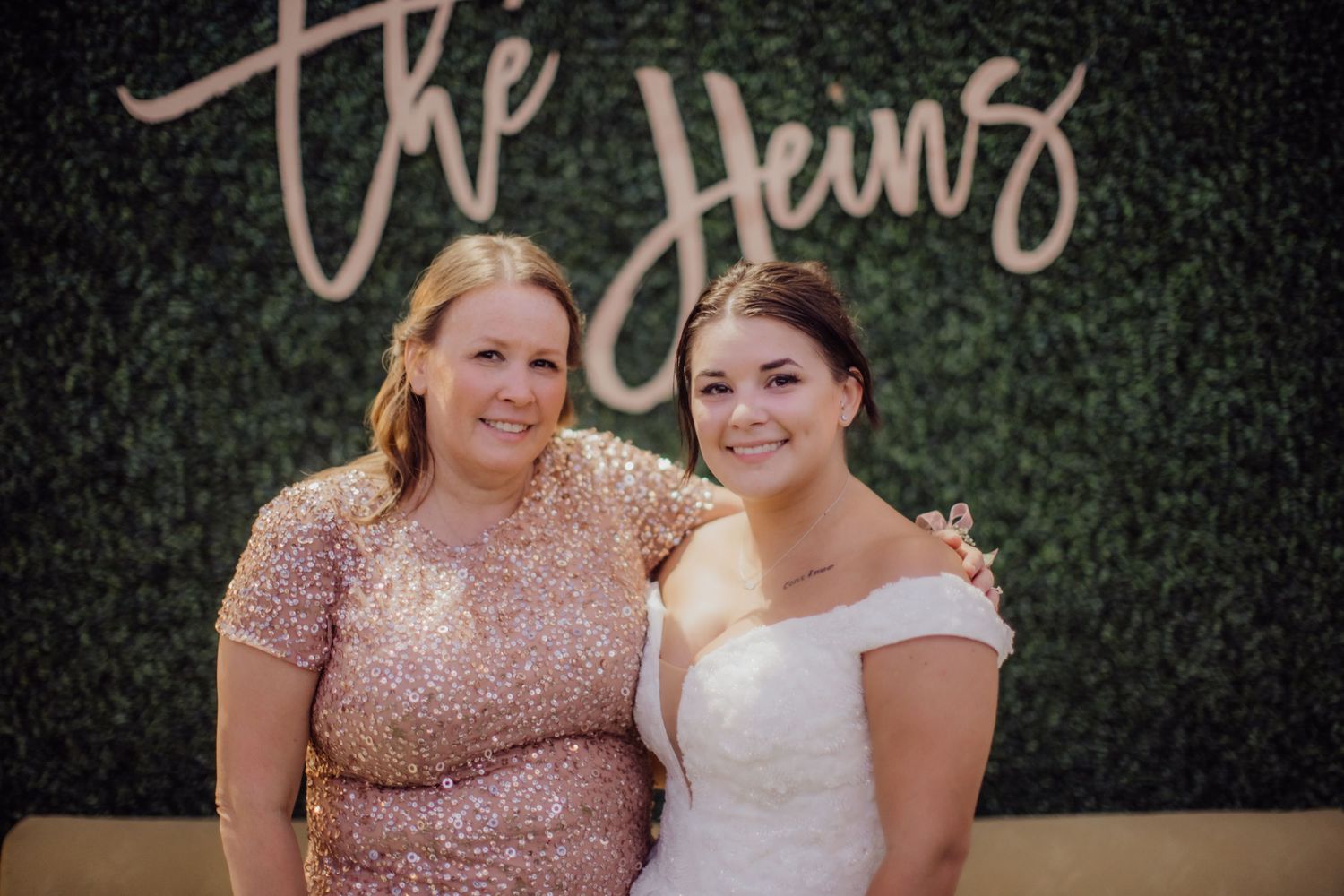 Wedding party members posing in front of a decorative green wall with script signage.