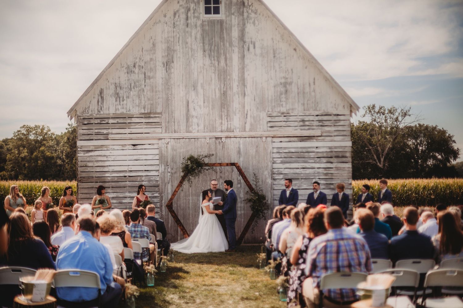 Rustic barn wedding ceremony setup with guests seated on white chairs.