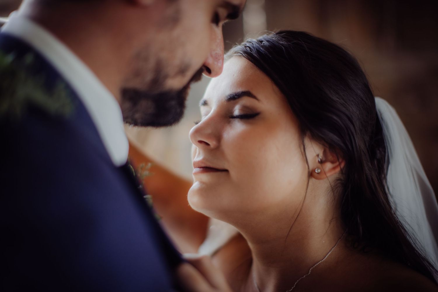 Romantic side profile of newlyweds sharing an intimate moment in rustic barn setting.