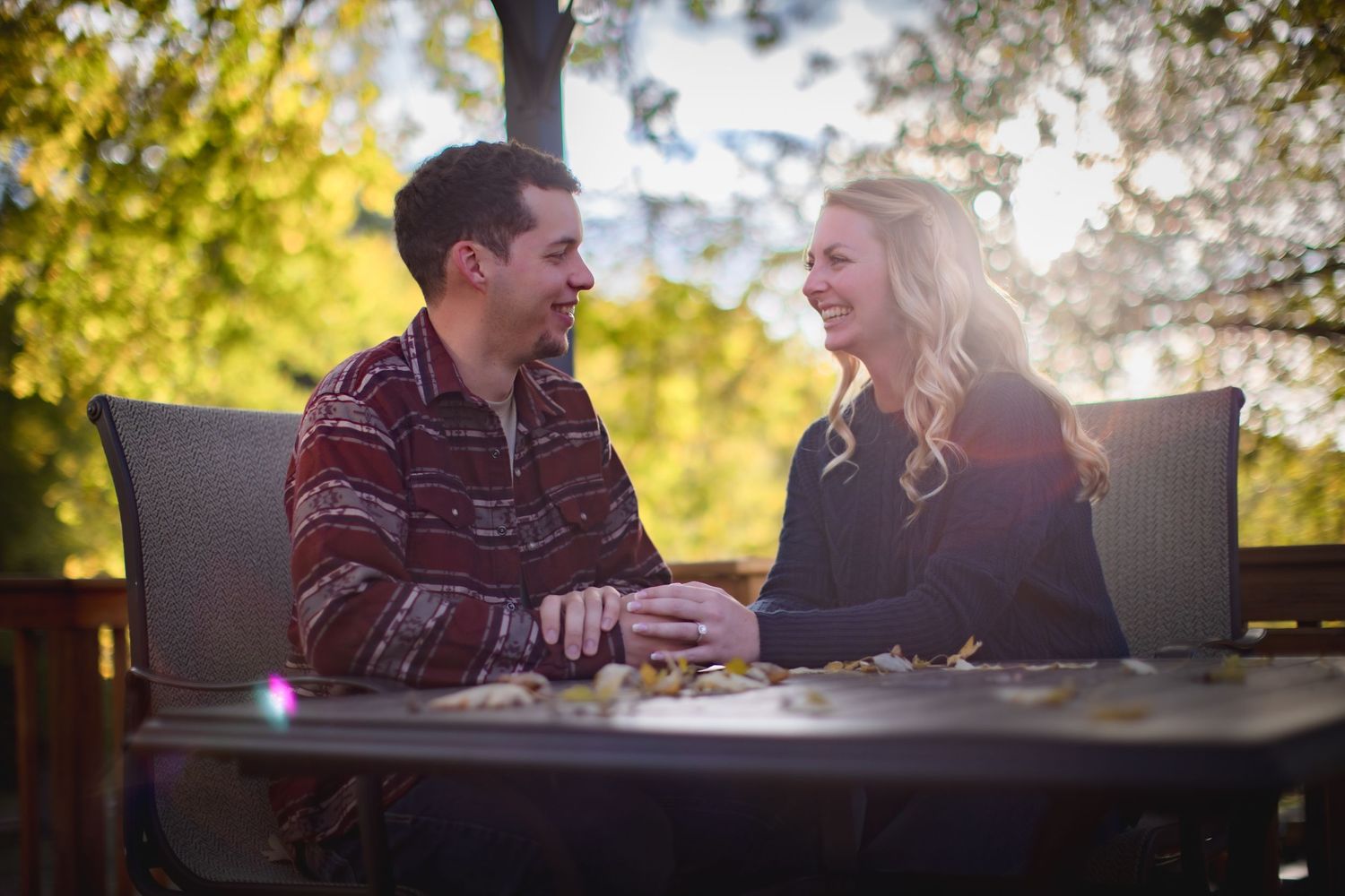 Couple enjoying conversation at sunset on wooden deck with autumn foliage.